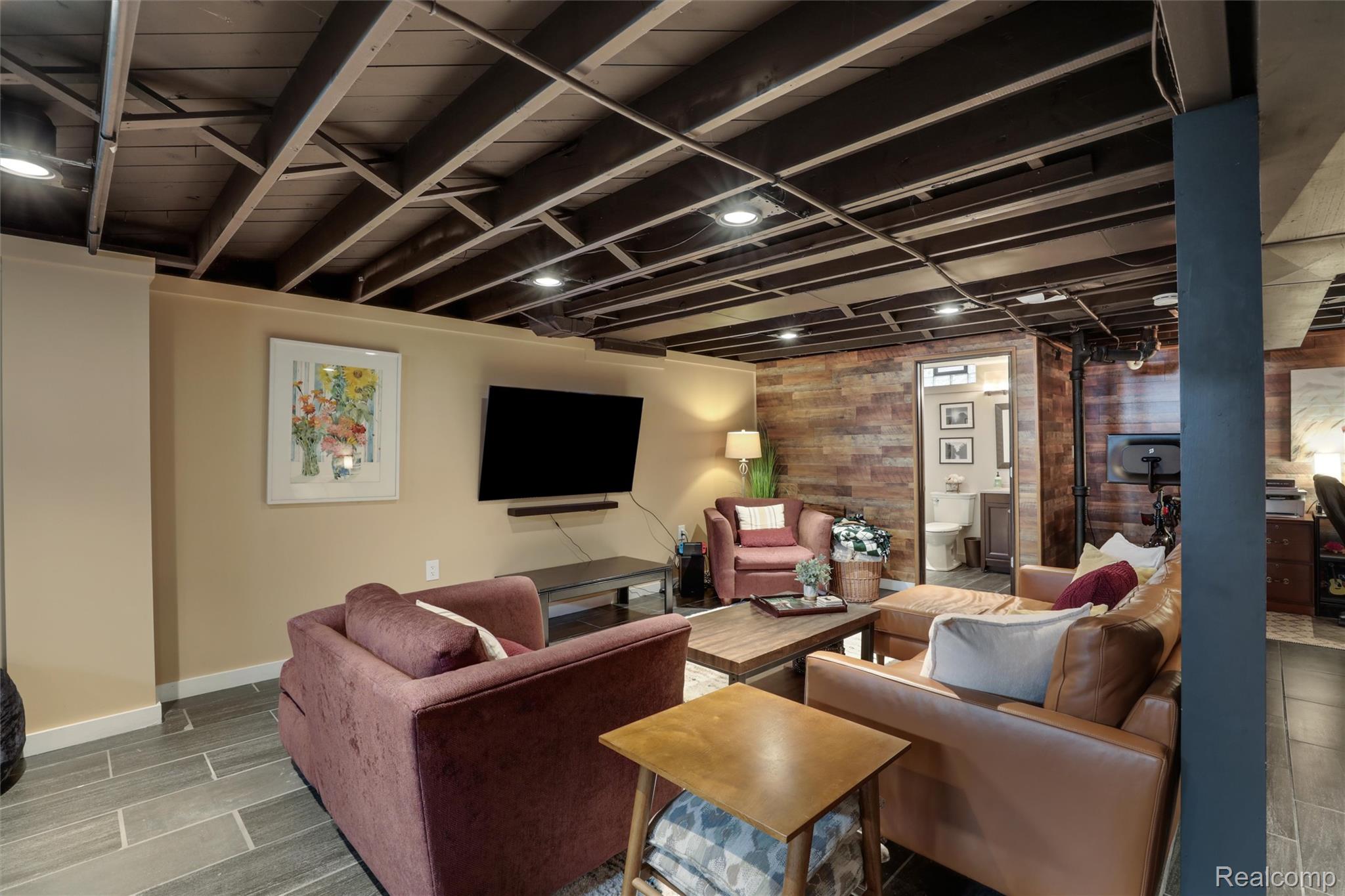 Basement living room with mauve seating, wood accent walls, and an exposed beam ceiling.