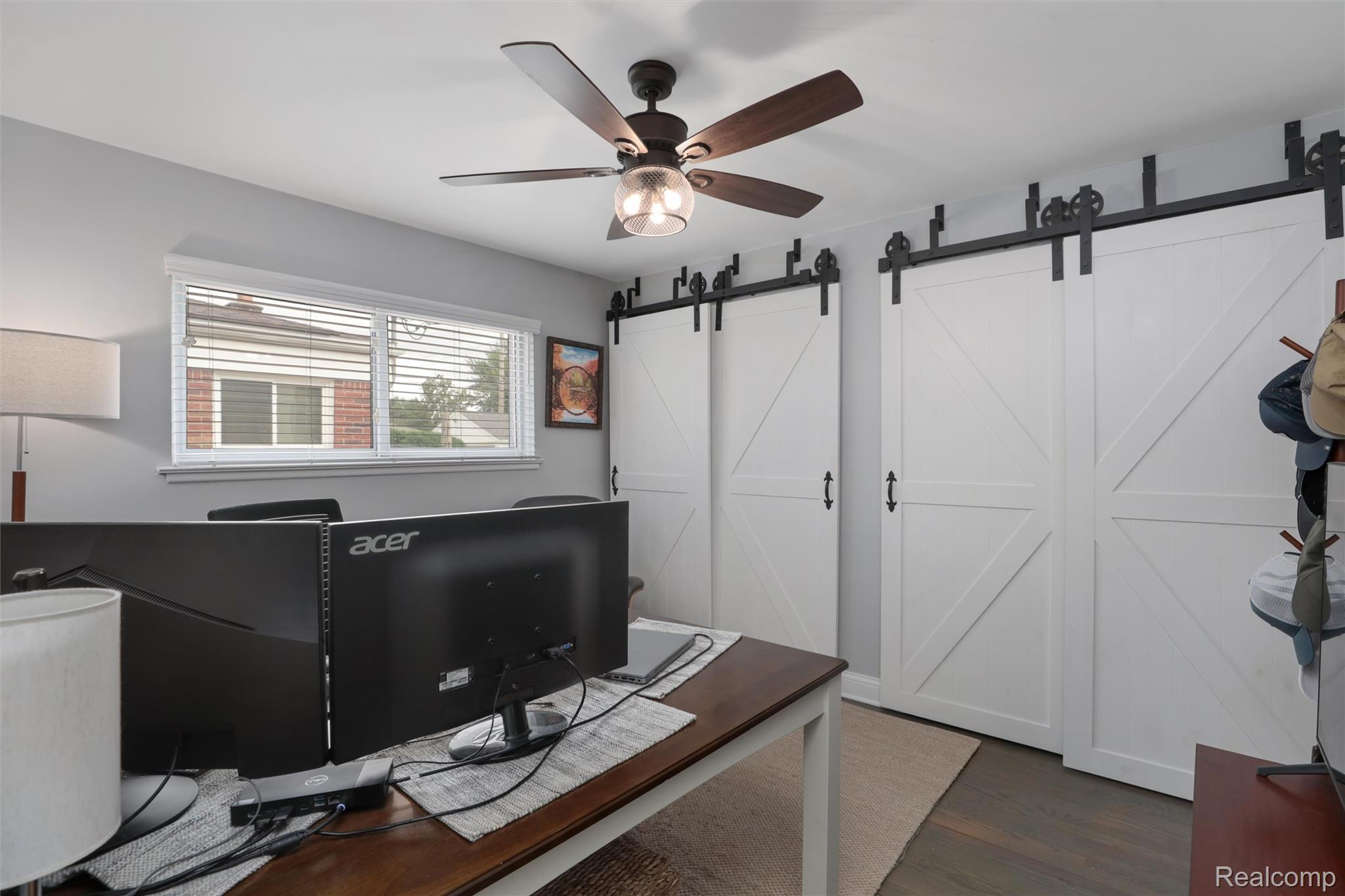 Home office with white sliding barn doors, a wooden desk, and a ceiling fan.
