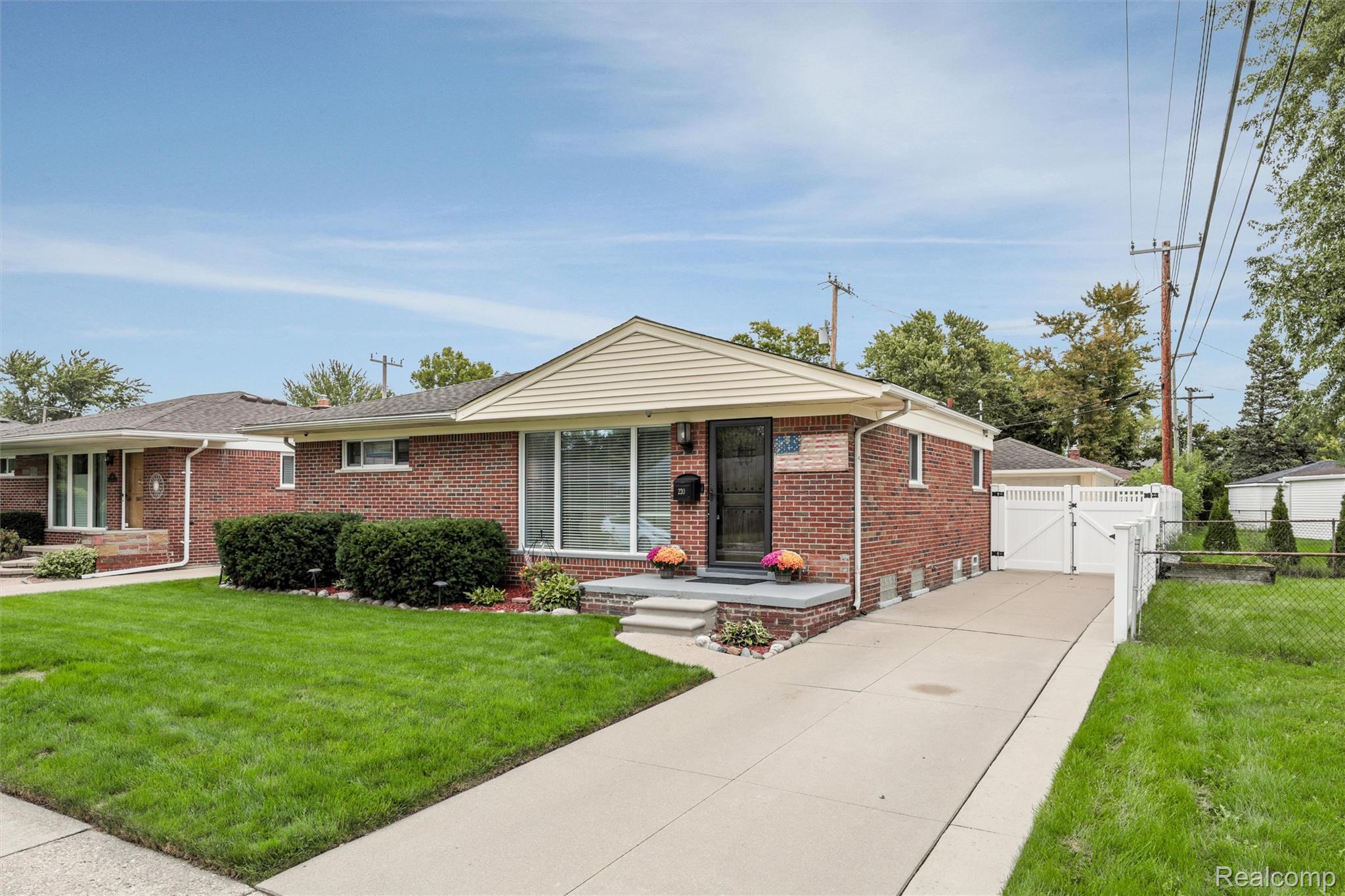 Red-brick ranch house with a broad front window, green lawn, and concrete driveway.