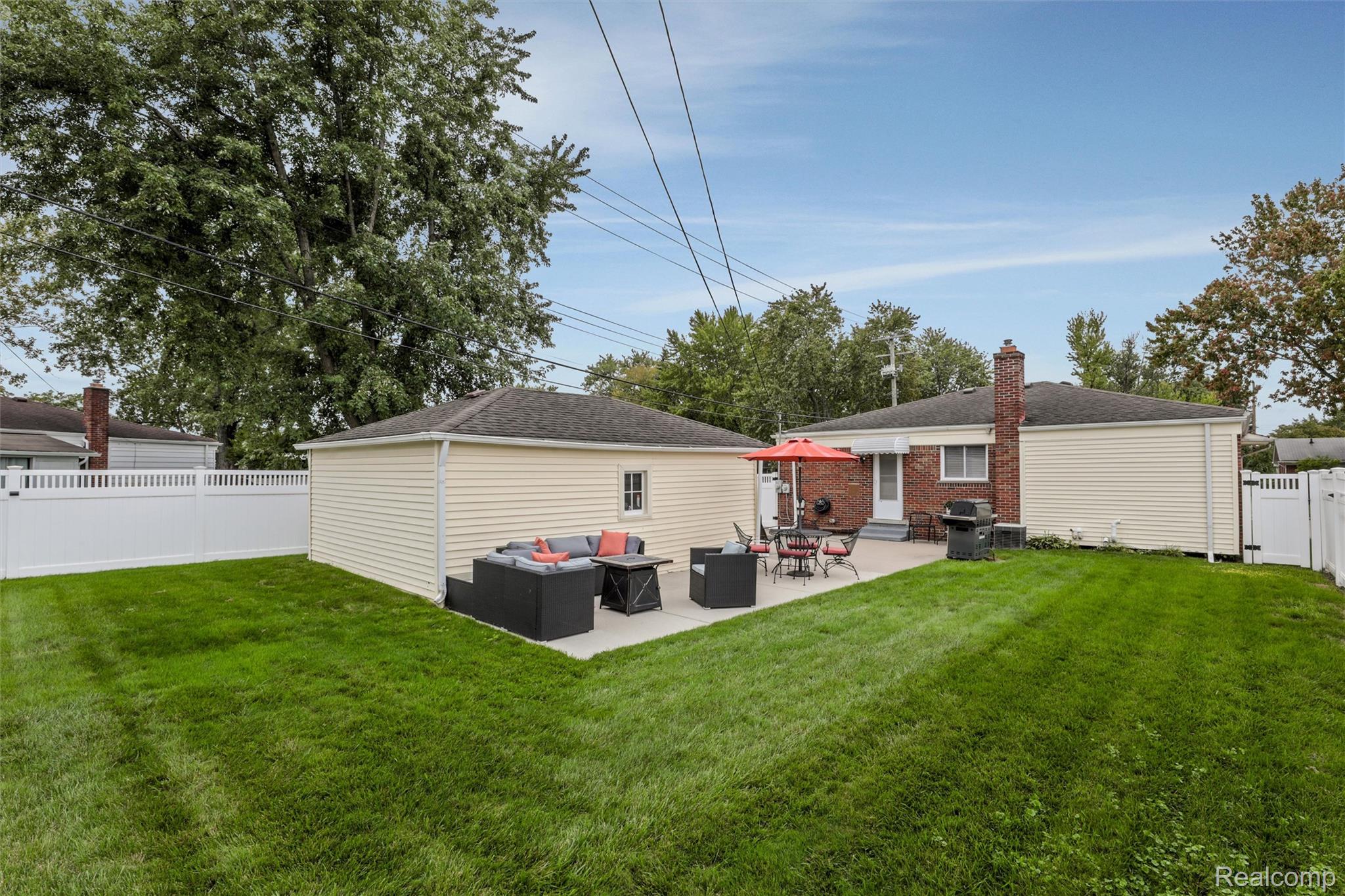 Home’s fenced backyard with a broad lawn and furnished patio under a red umbrella.