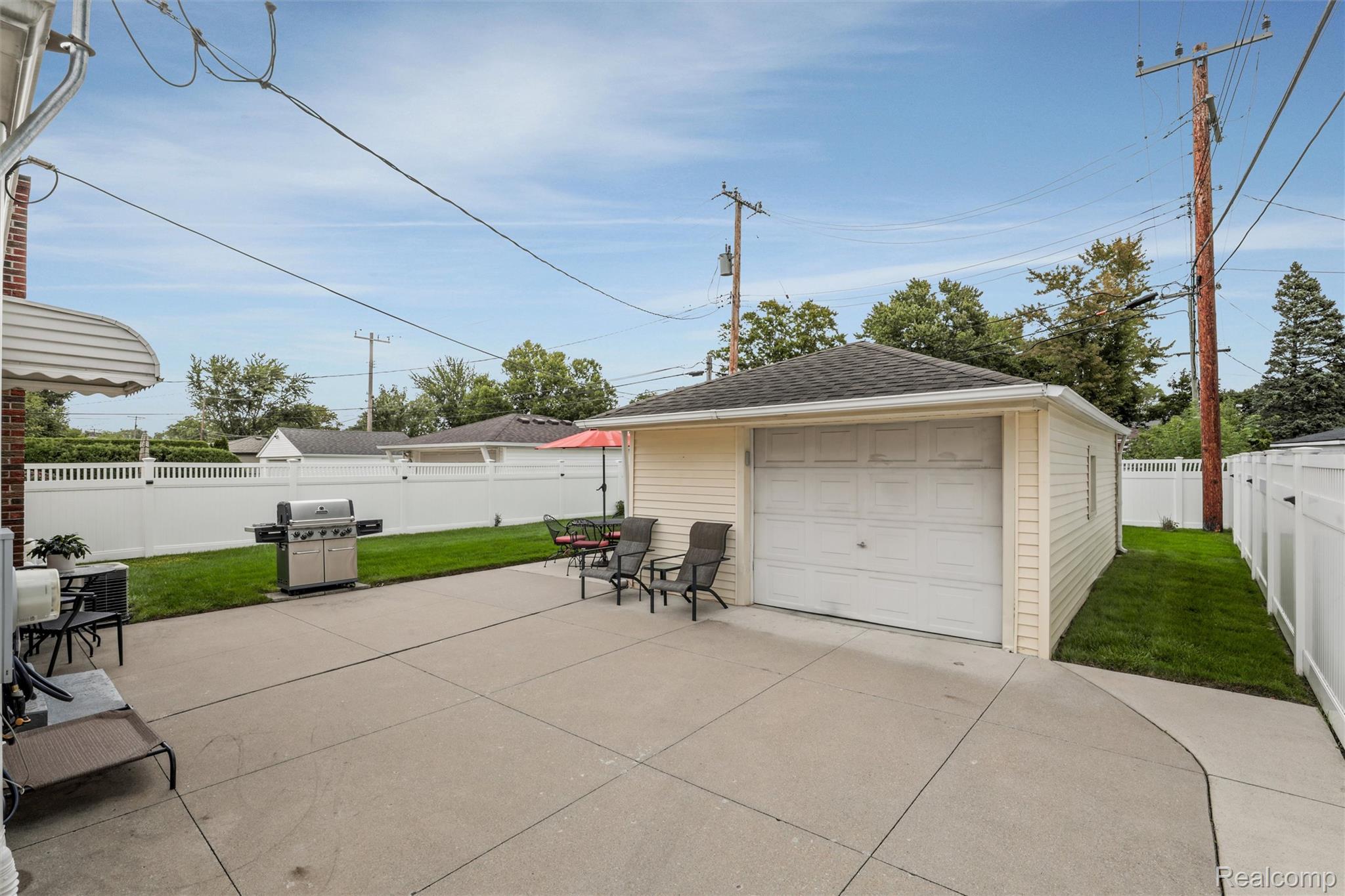 Backyard patio with a detached garage, concrete seating area, grill, and white privacy fence.