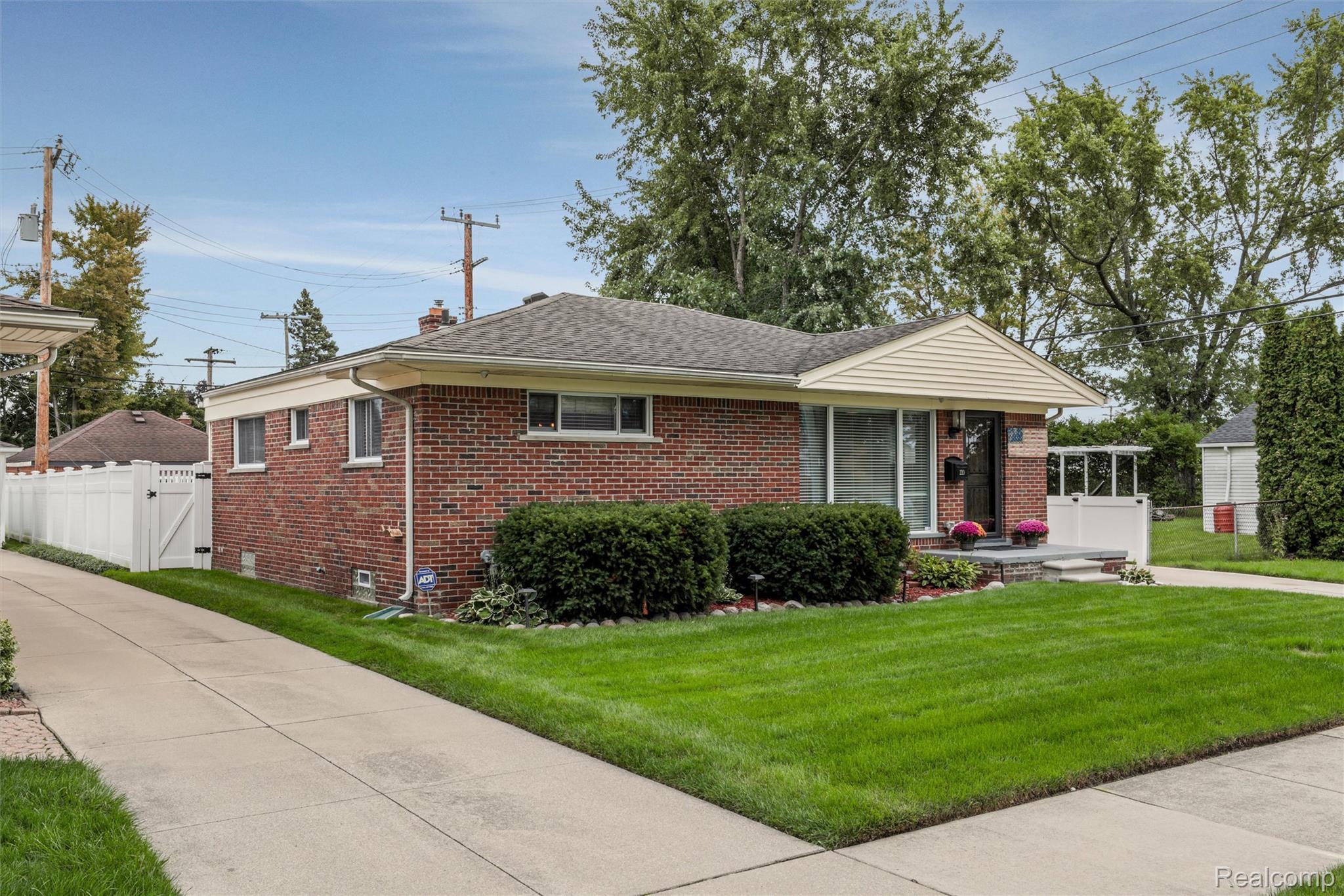 Single-story brick house with white trim, a manicured lawn, and white privacy fencing.