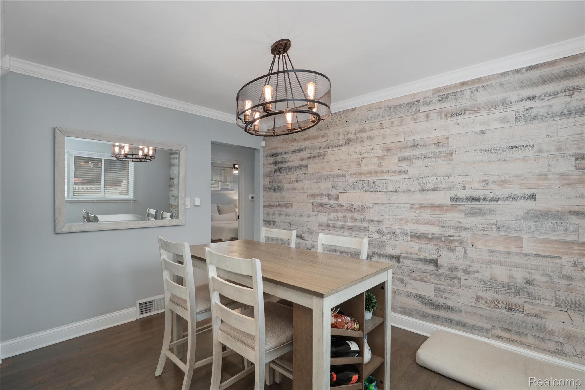Dining area with white chairs, a rustic plank accent wall, and a circular metal chandelier.