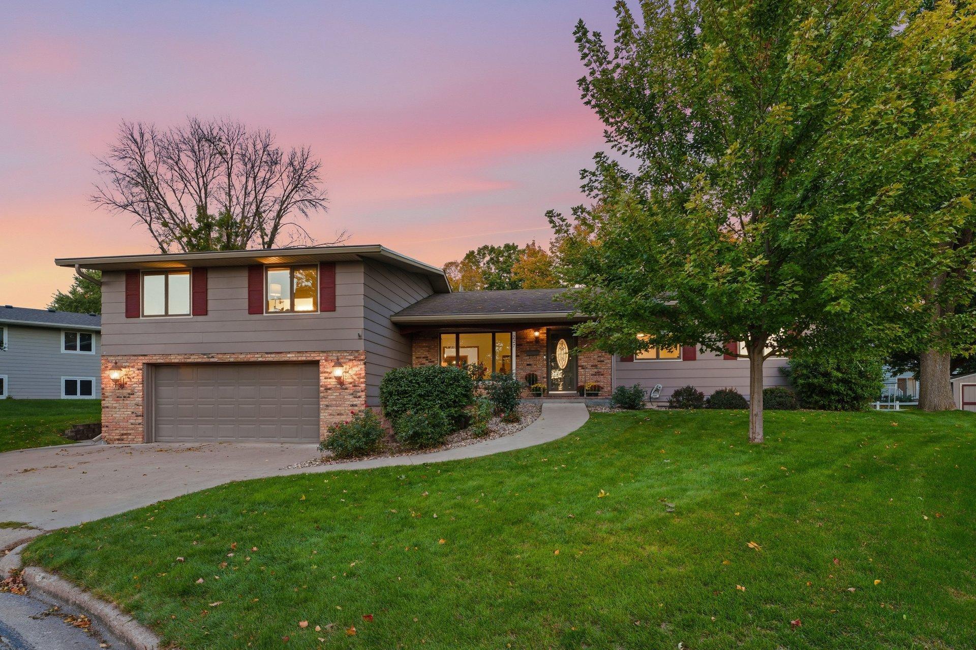 Split-level home with brick and gray siding, a double garage, and a pink dusk sky.