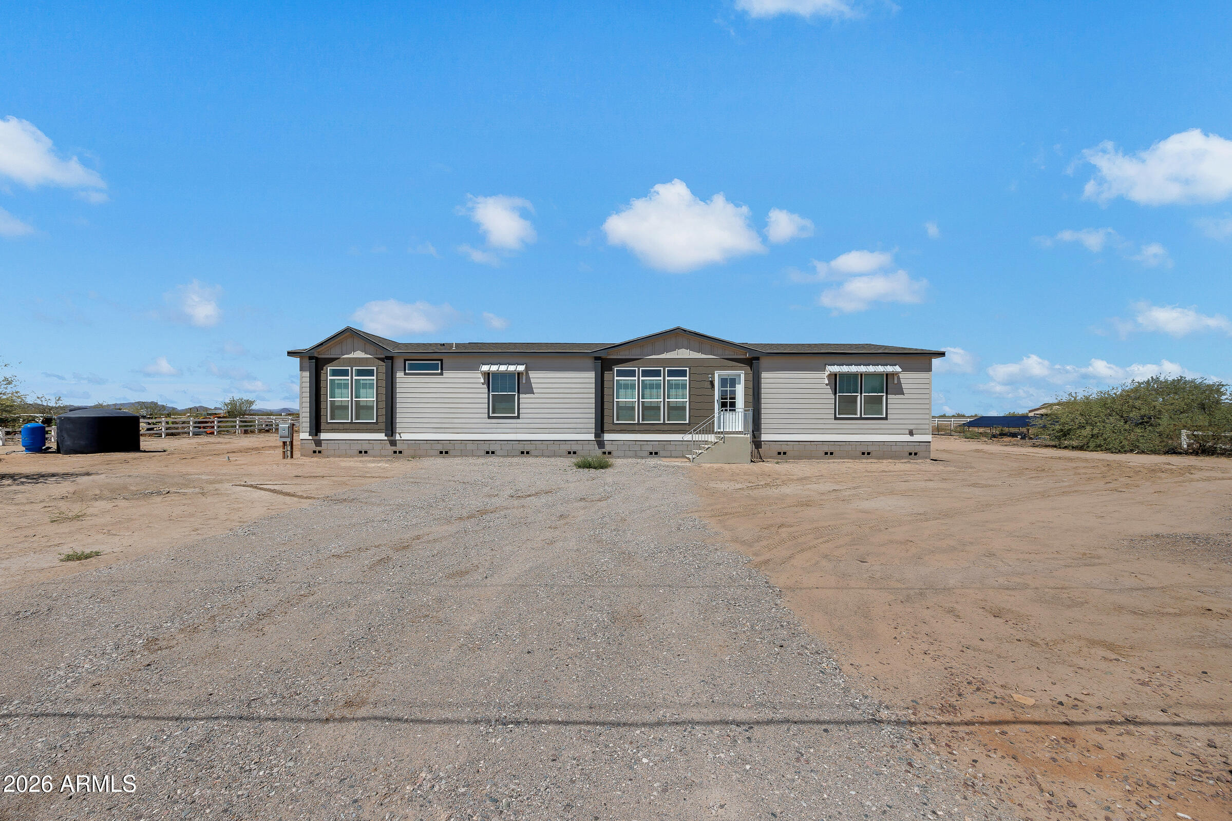 Single-story gray home with dark trim on a broad gravel and dirt lot.