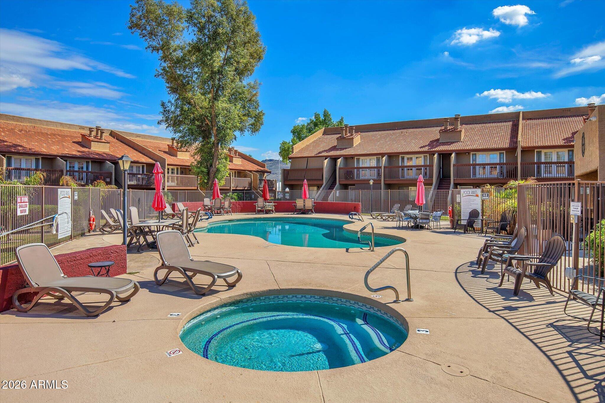 Community pool and spa with lounge chairs and red umbrellas, surrounded by two-story apartment buildings.