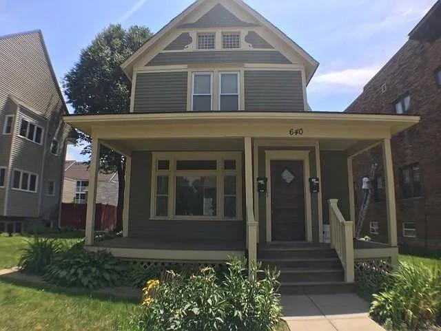 Two-story gray house with a covered porch, cream trim, and a small front garden.