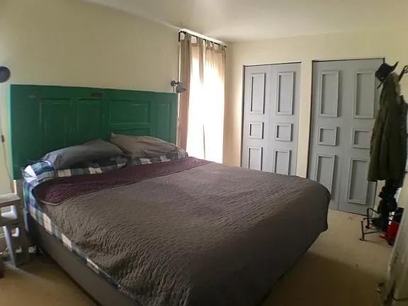 Bedroom with a large bed, dark green paneled headboard, and white closet doors.