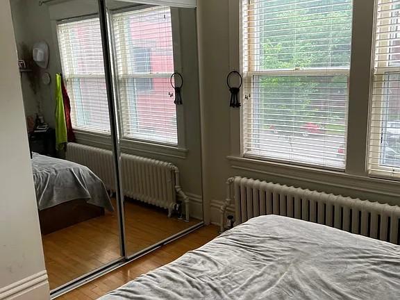 Bedroom with mirrored closet doors, hardwood floors, and multiple windows above radiators.