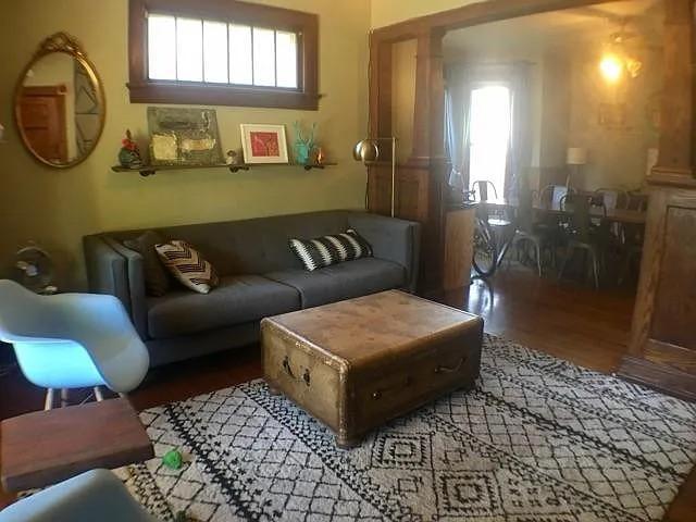 Living room with a gray sofa, vintage trunk coffee table, and geometric rug beside an open dining area.