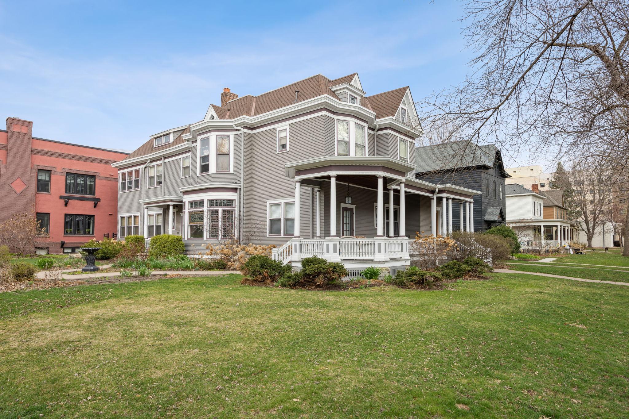 Gray Victorian-style home with white trim, bay windows, and a wraparound porch overlooking a broad lawn.