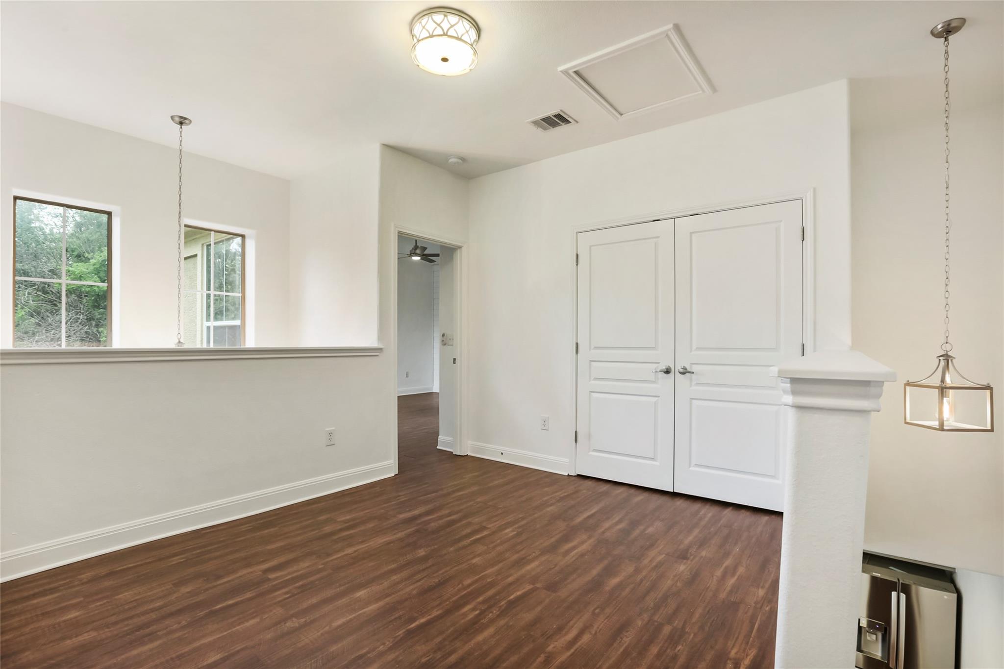 Vacant interior with dark wood-look floors, white double doors, and a half wall overlooking a lower level.