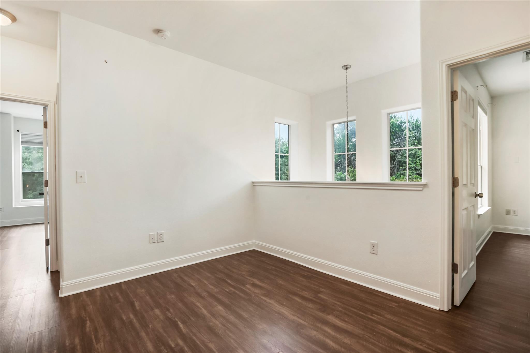 Empty room with dark wood floors, three windows, and a pass-through ledge.