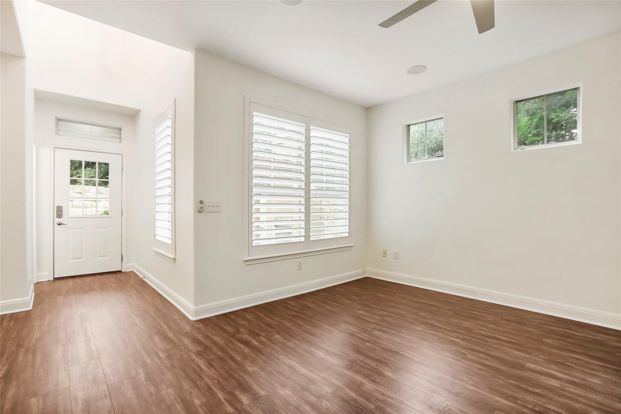 Vacant interior room with wood-look flooring, plantation shutters, and a glass-paneled entry door.