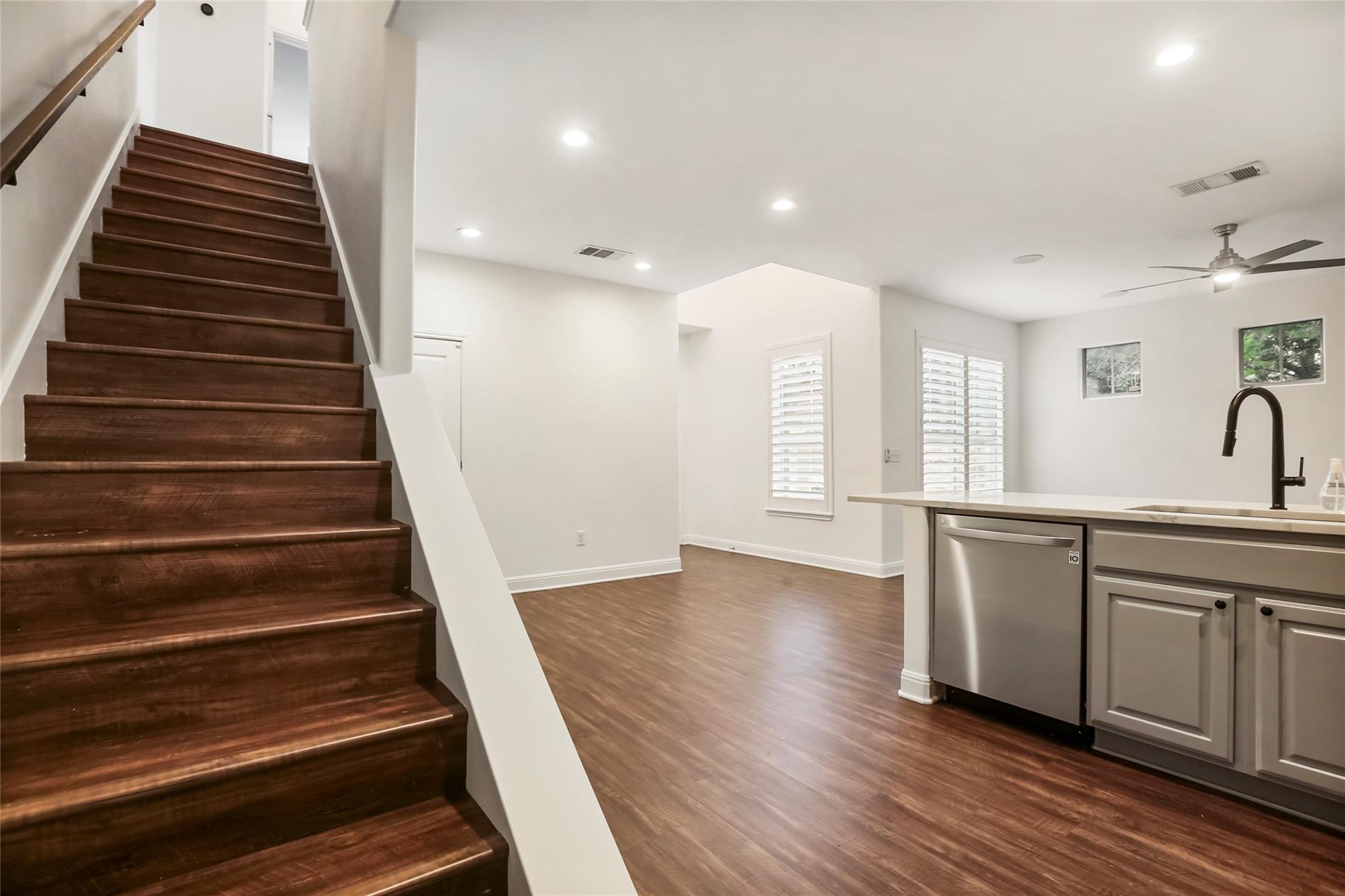 Open-plan kitchen and staircase with dark wood steps, gray cabinets, and stainless steel dishwasher.
