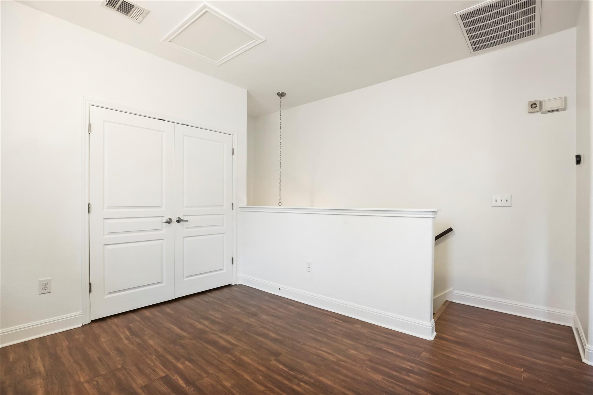 Empty landing with dark wood flooring, white double doors, and a half-height stair railing.