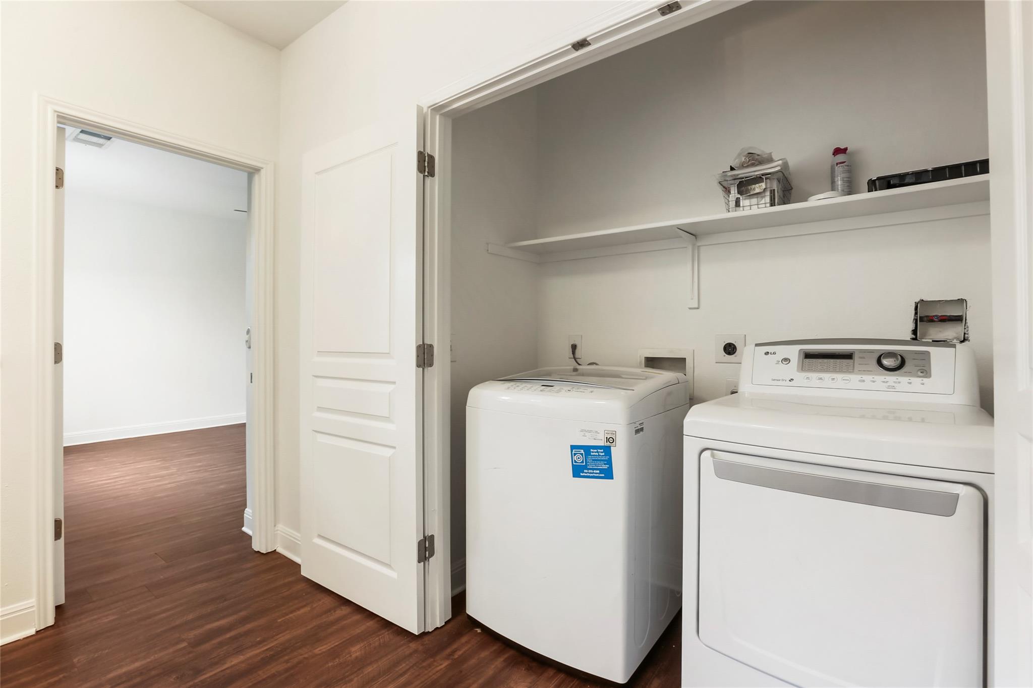 Laundry closet with a top-loading washer, front-loading dryer, and open shelves.