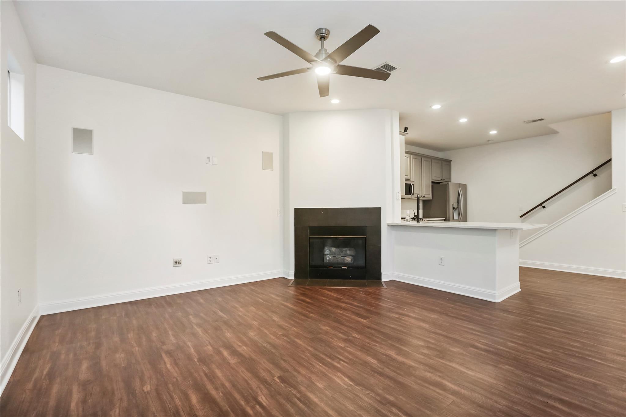 Empty living room with wood-look floors, a black fireplace, and an open kitchen and staircase.