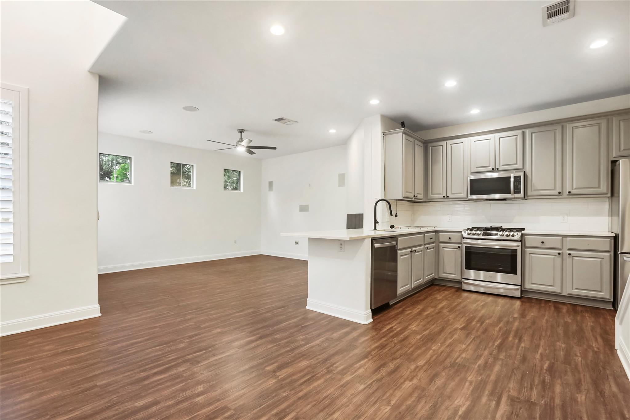 Open kitchen and living area with gray cabinets, stainless steel appliances, and brown wood-look flooring.