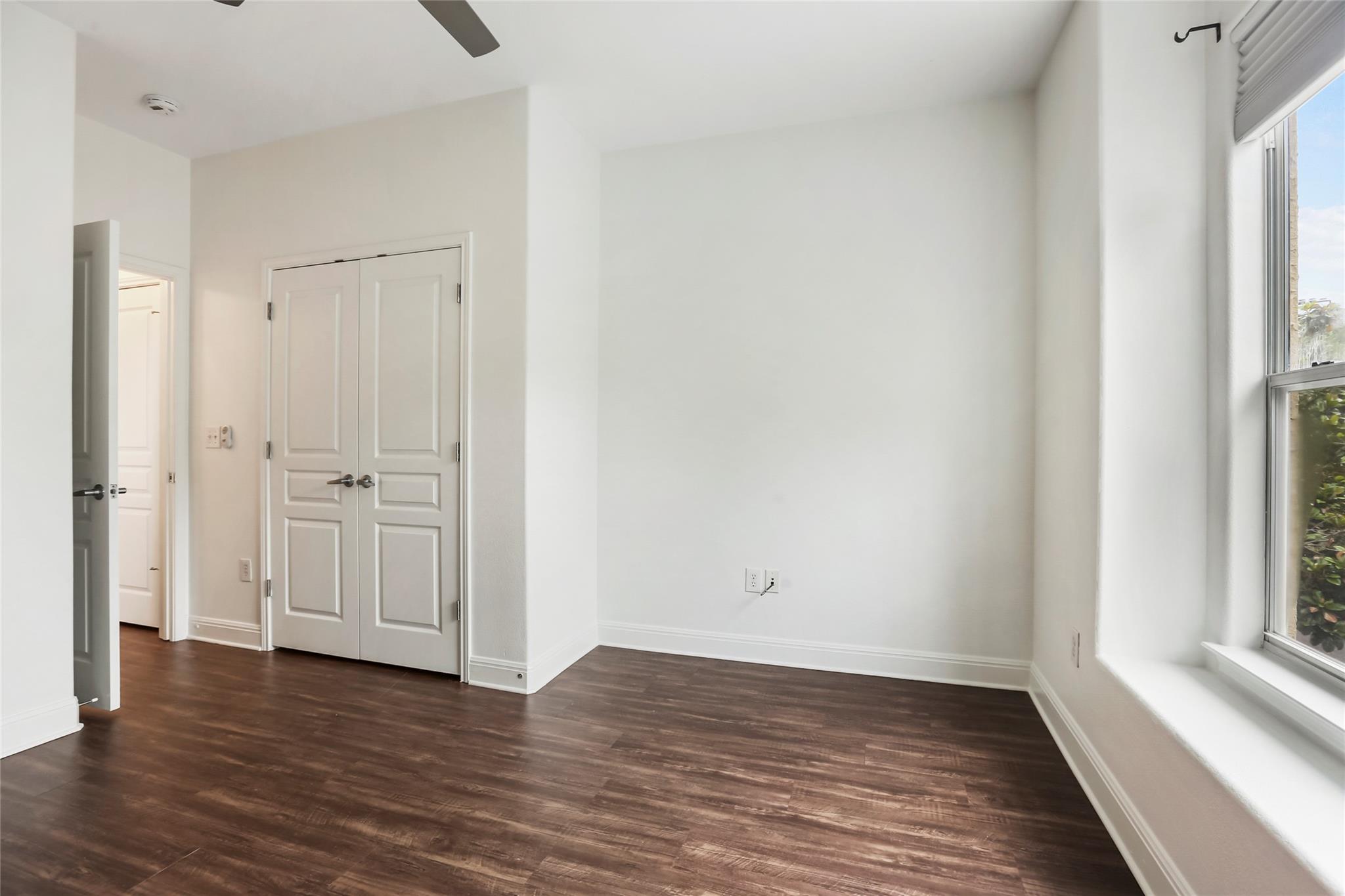 Empty room with dark wood floors, double closet doors, and a large window with a deep sill.