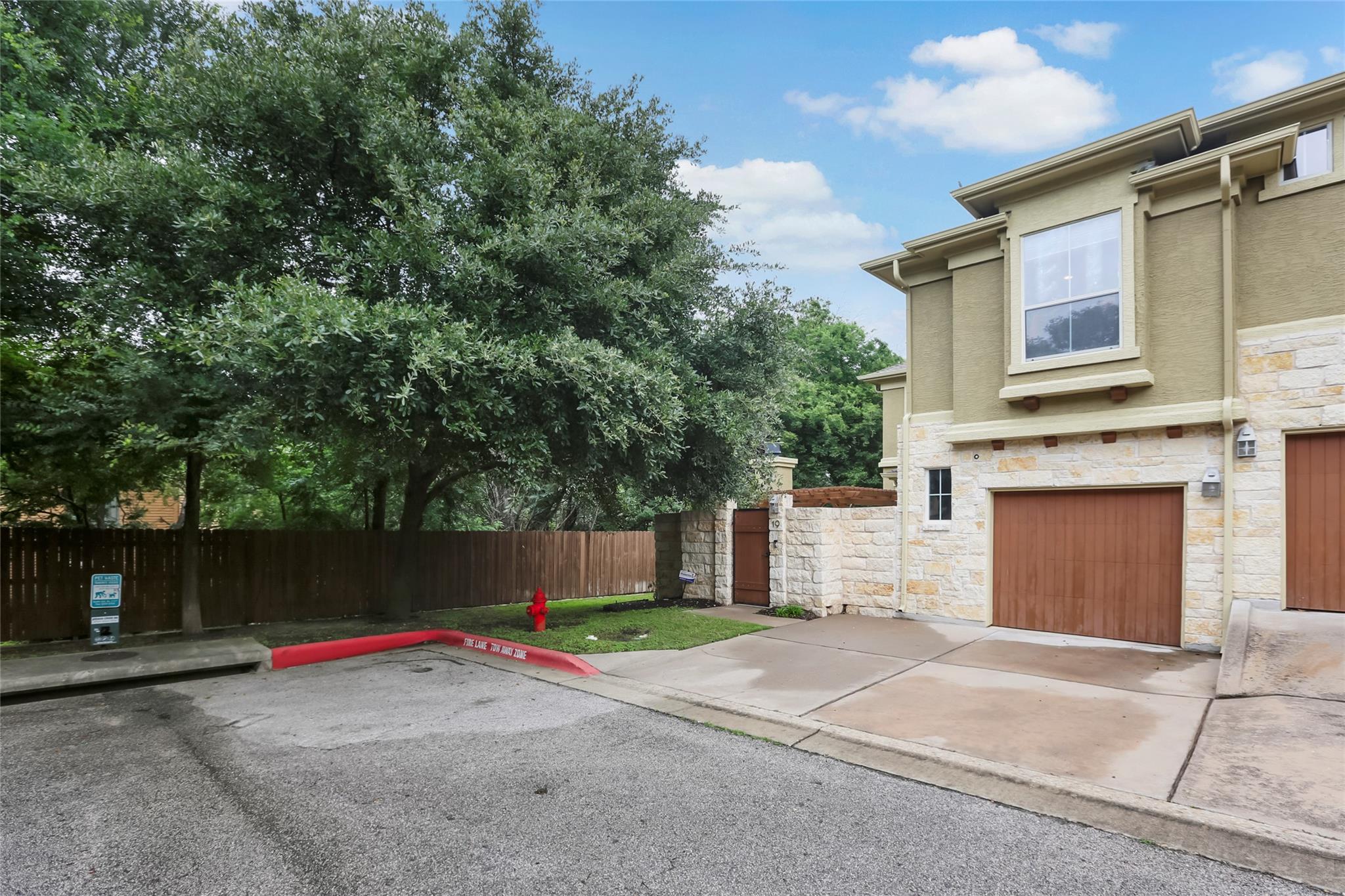 Two-story townhouse with stone facade, brown garage door, concrete driveway, and mature trees.
