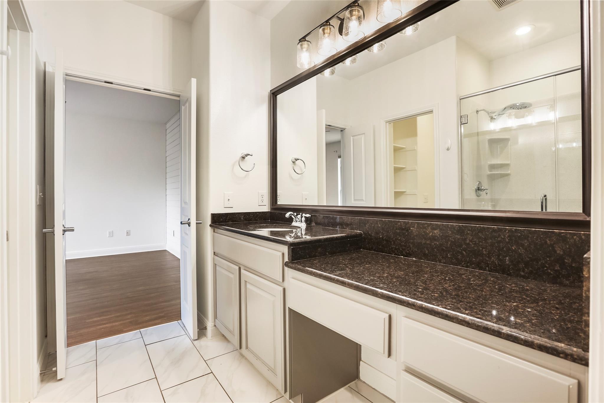 Bathroom with a long dark stone vanity, large framed mirror, and glass-enclosed shower.