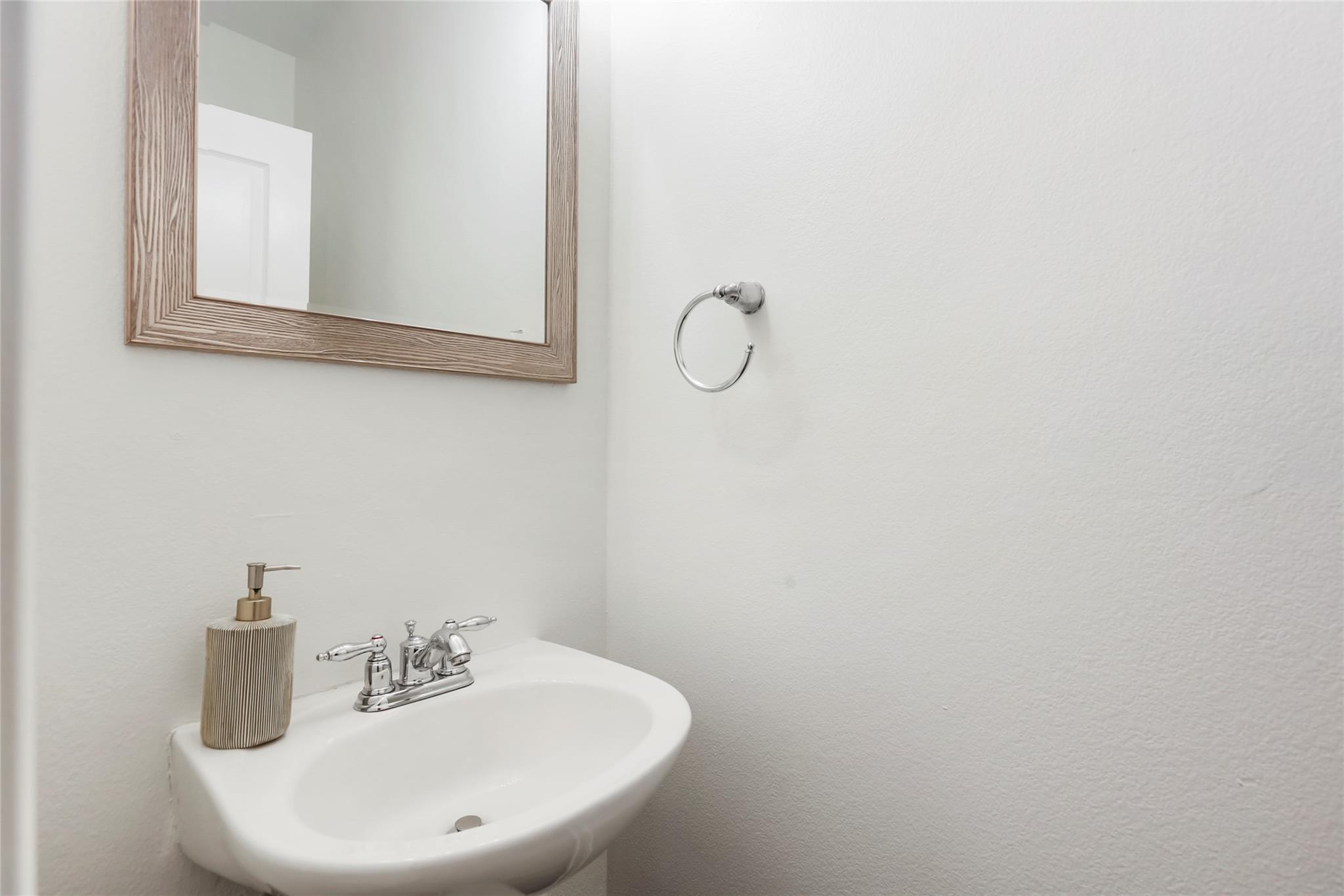 Bathroom sink with chrome faucet, wood-framed mirror, and soap dispenser.