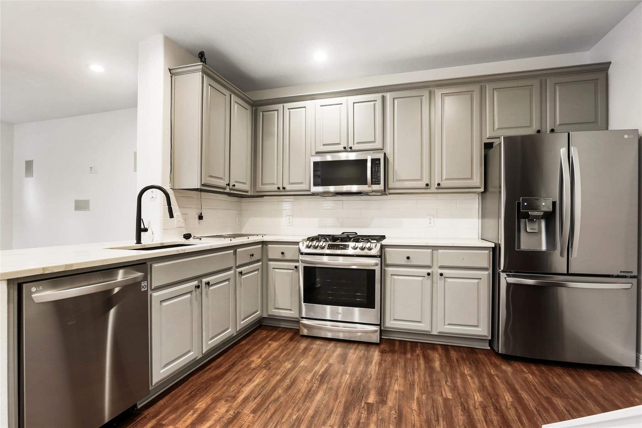 Kitchen with gray cabinets, stainless steel appliances, white counters, and dark wood flooring.