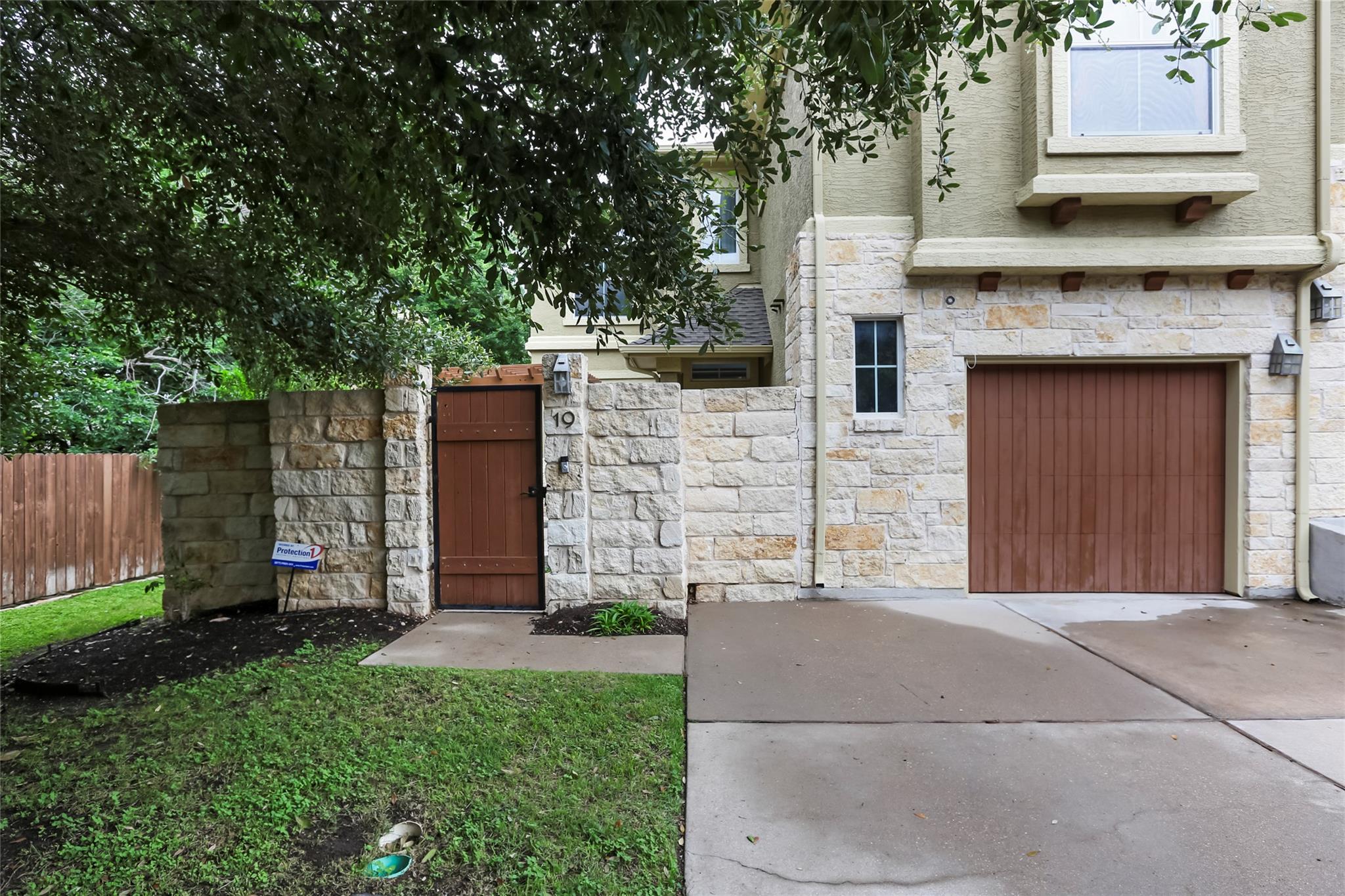 Stone-front residence with a reddish-brown garage door and gated entry marked 19.