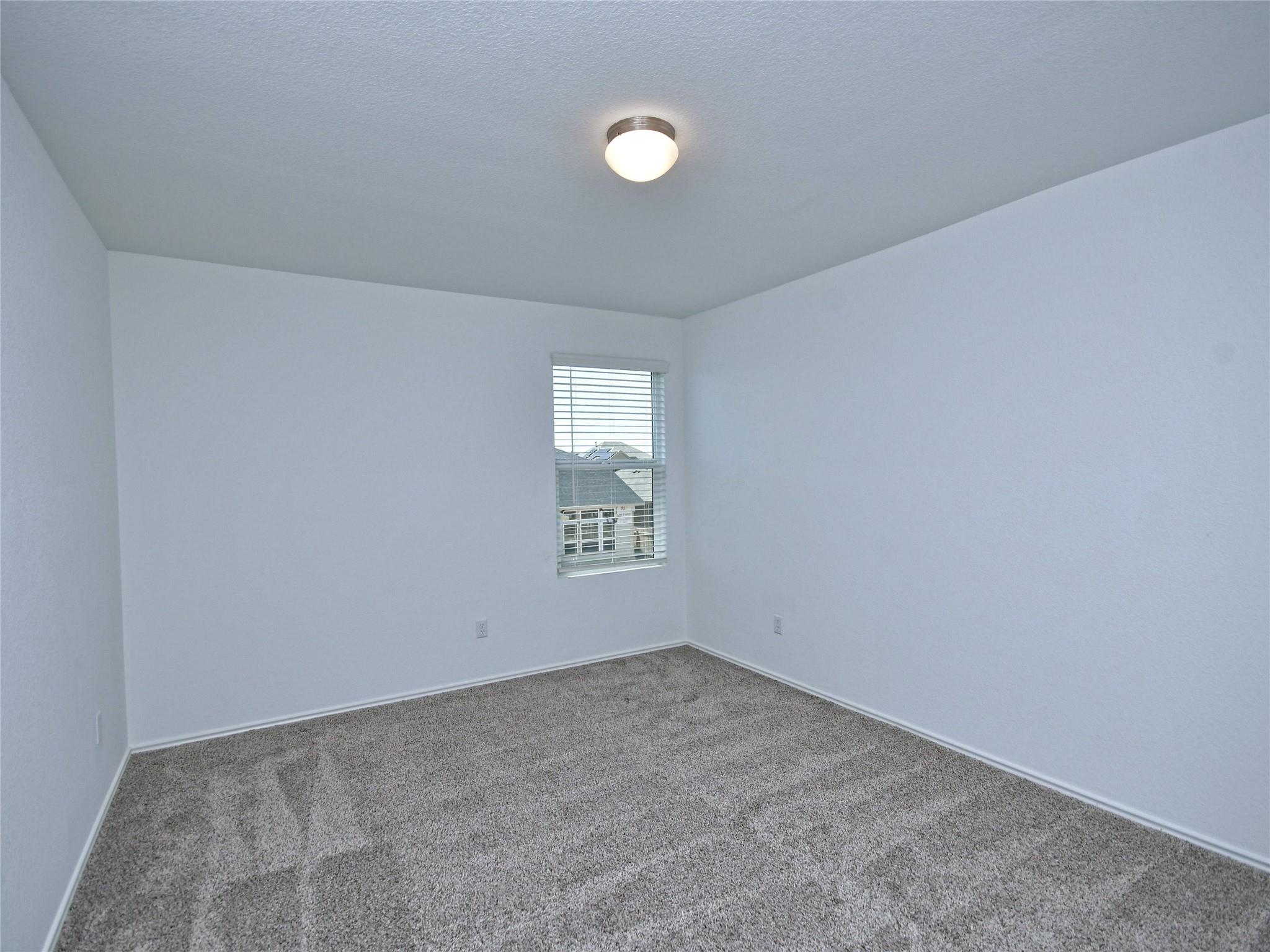 Empty bedroom with gray carpet and a window fitted with blinds.