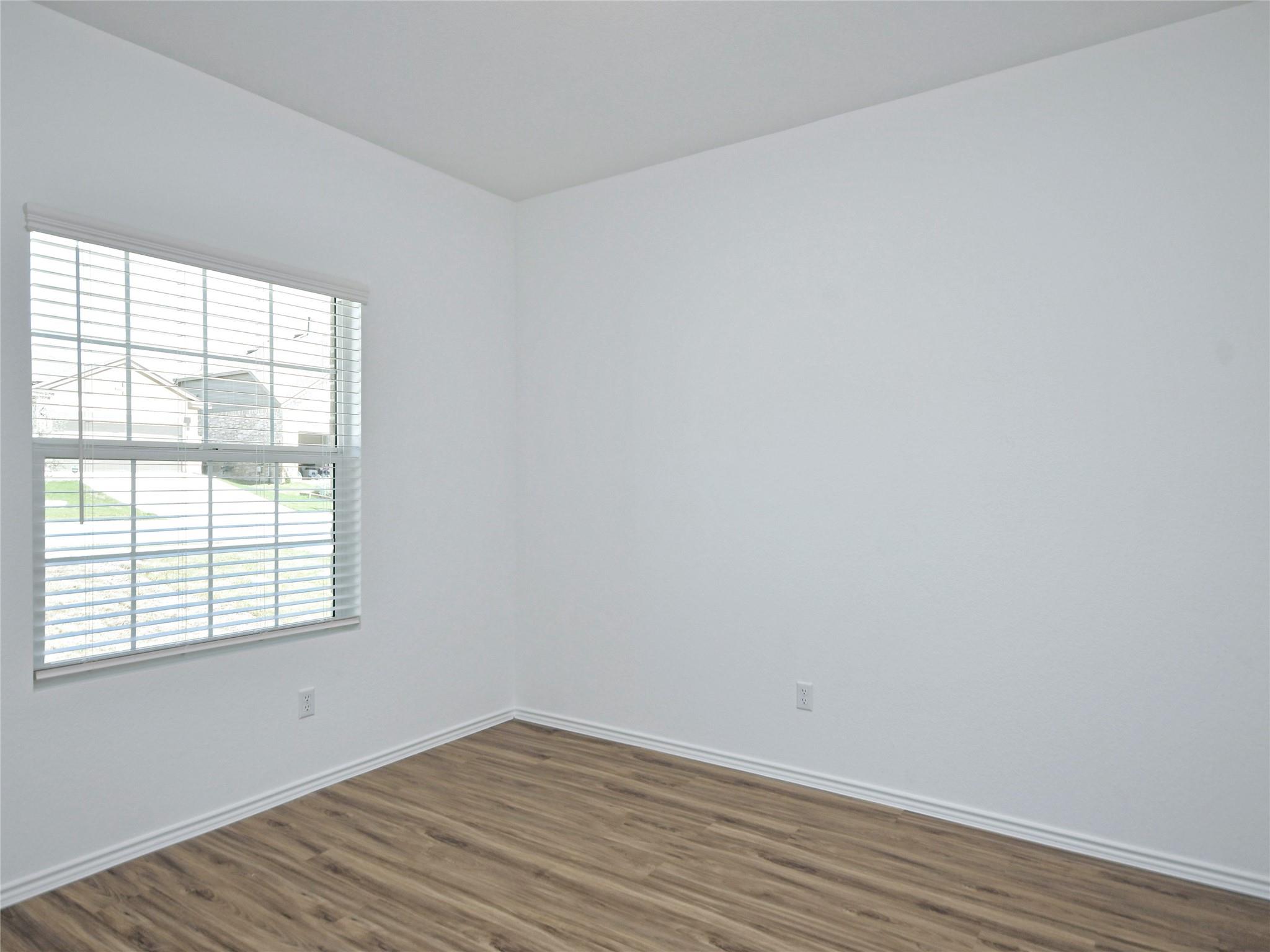 Empty room with wood-look flooring, white walls, and a window with blinds.