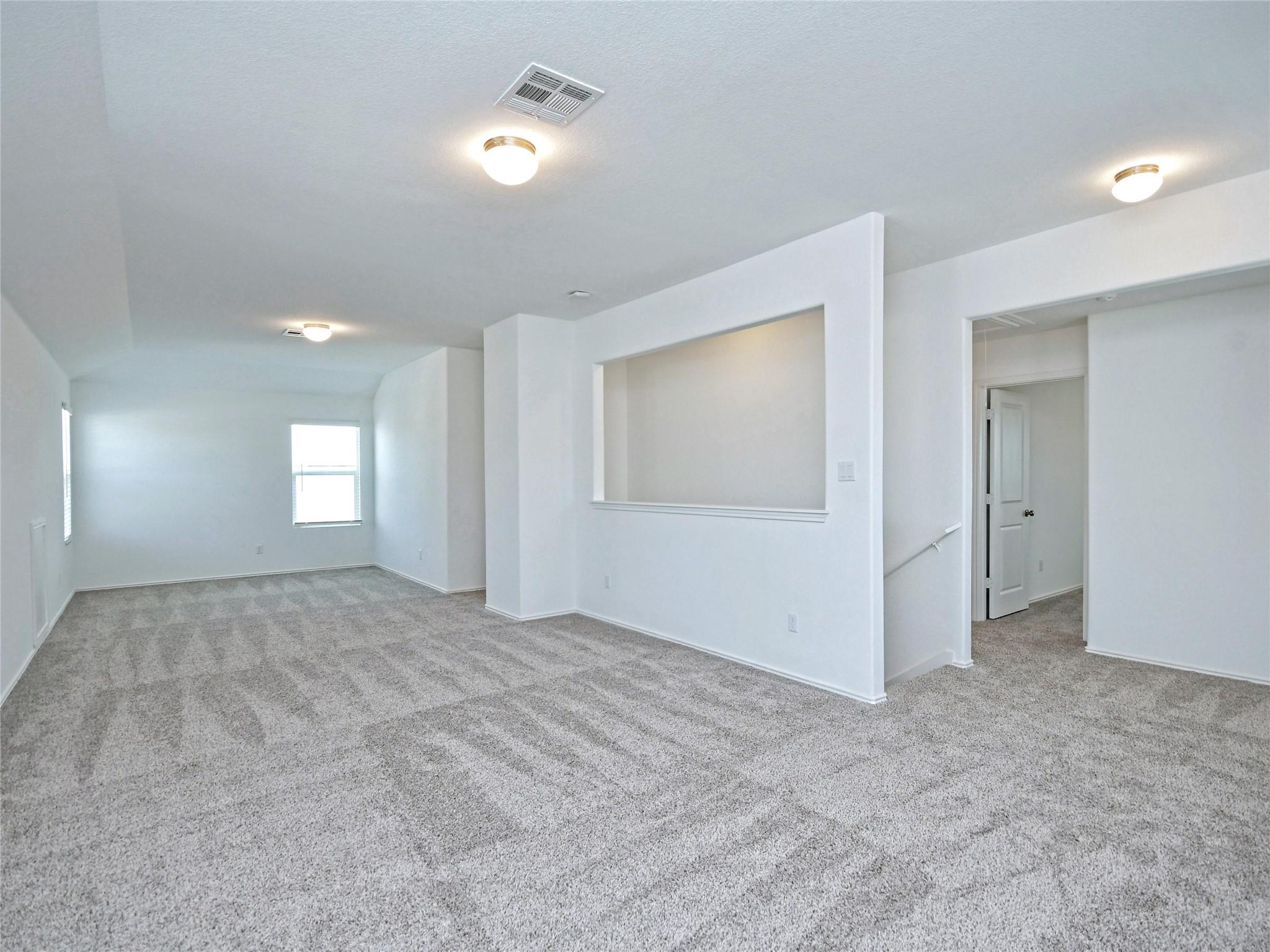 Empty carpeted living area with a wide pass-through opening and windows.