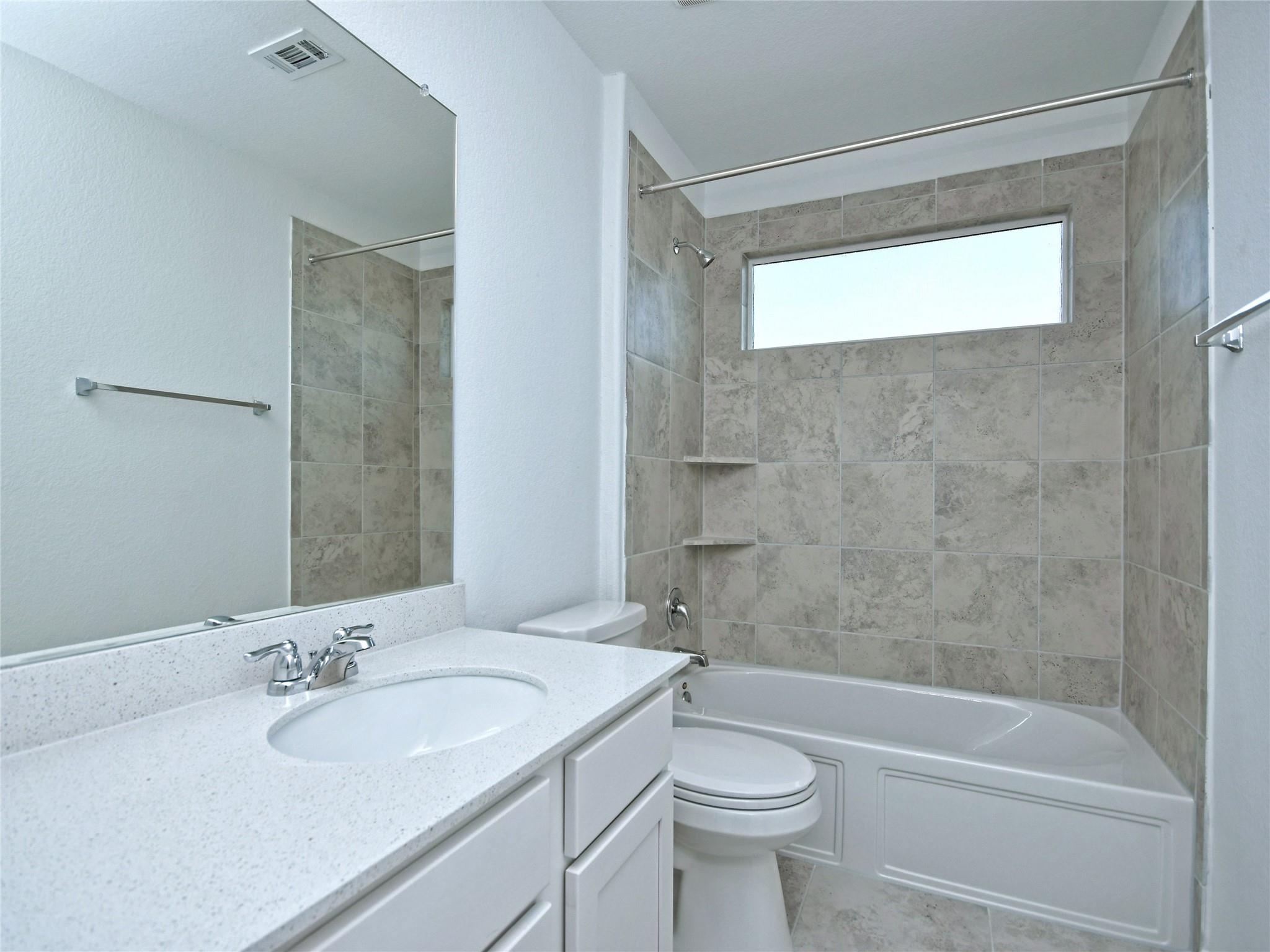 Bathroom with a white vanity, toilet, and tub beneath a narrow horizontal window.