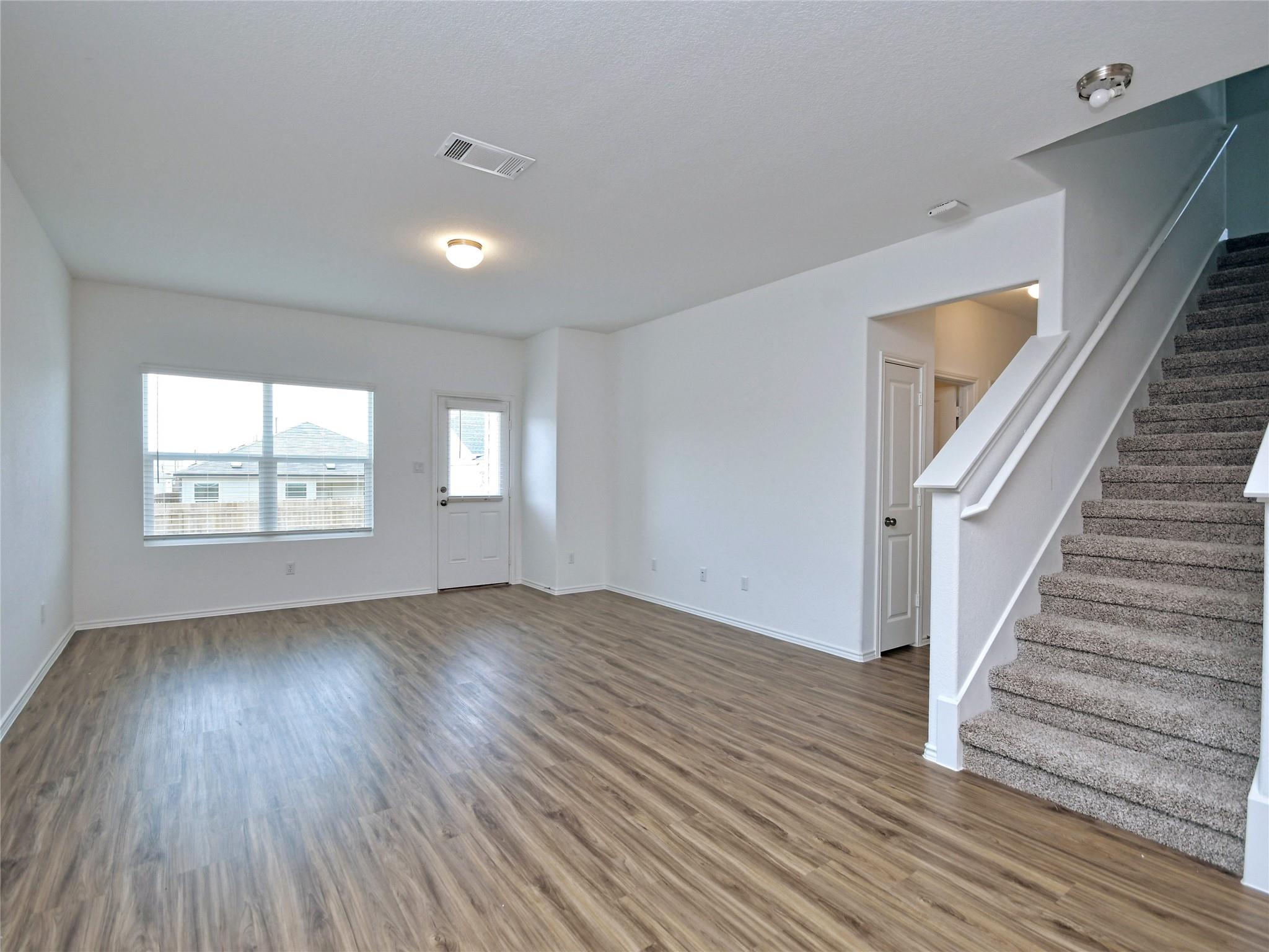 Vacant living area with wood-look floors, a window beside the front door, and a carpeted staircase.