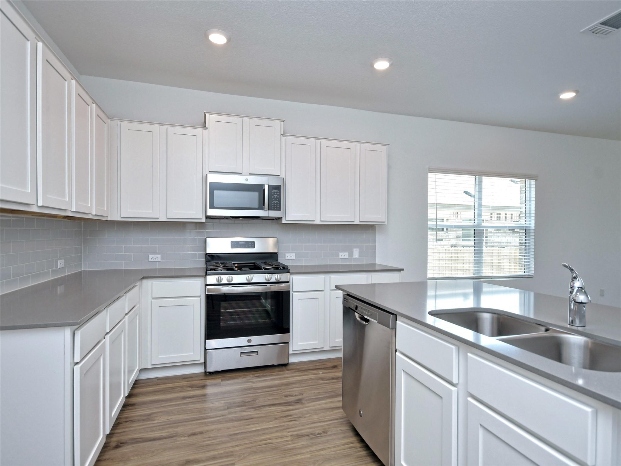 Kitchen with white shaker cabinets, stainless steel appliances, and a large island with a double sink.