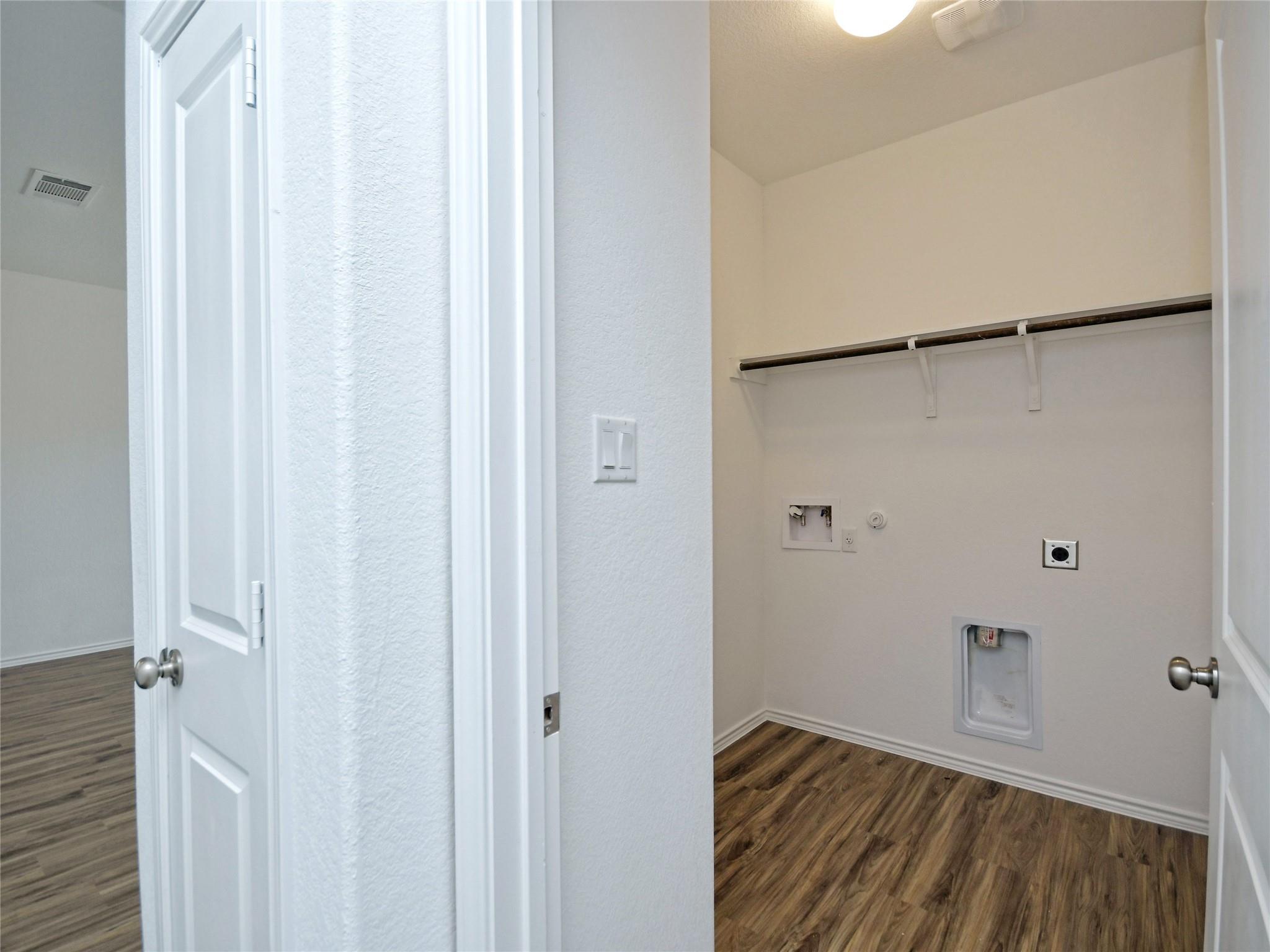 Empty laundry room with wood-look flooring, washer hookups, and a long shelf and hanging rod.