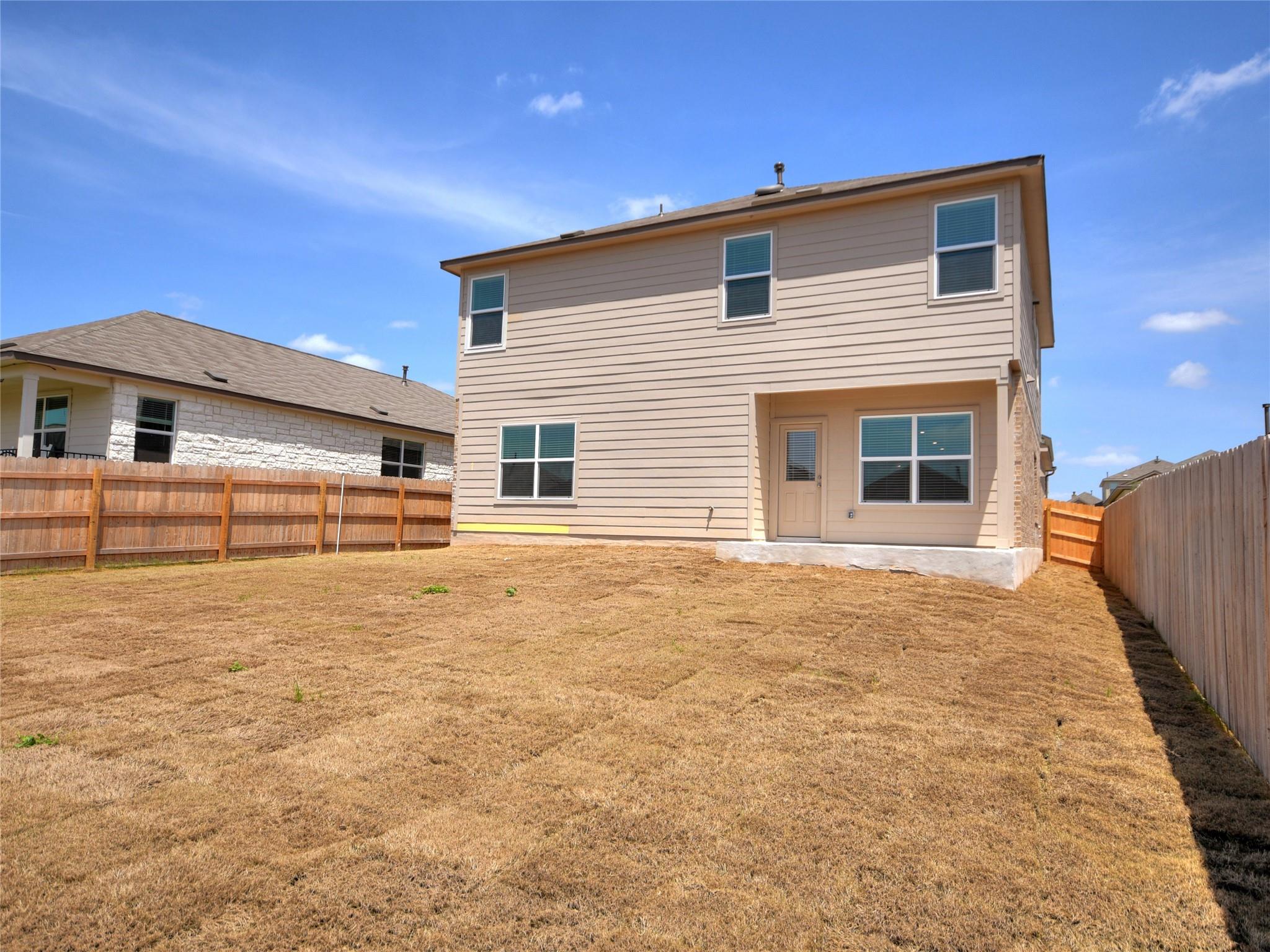 Two-story beige house with a covered patio and fenced, dry-grass backyard.