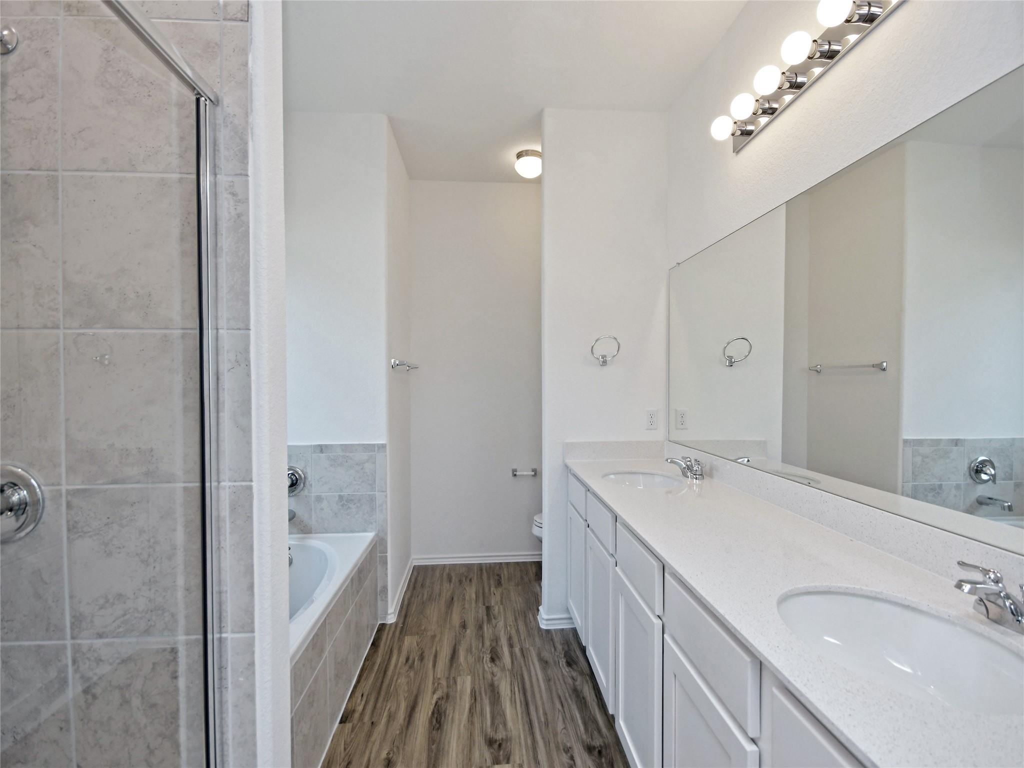 Bathroom with a long double-sink vanity, large mirror, and tiled tub and shower.