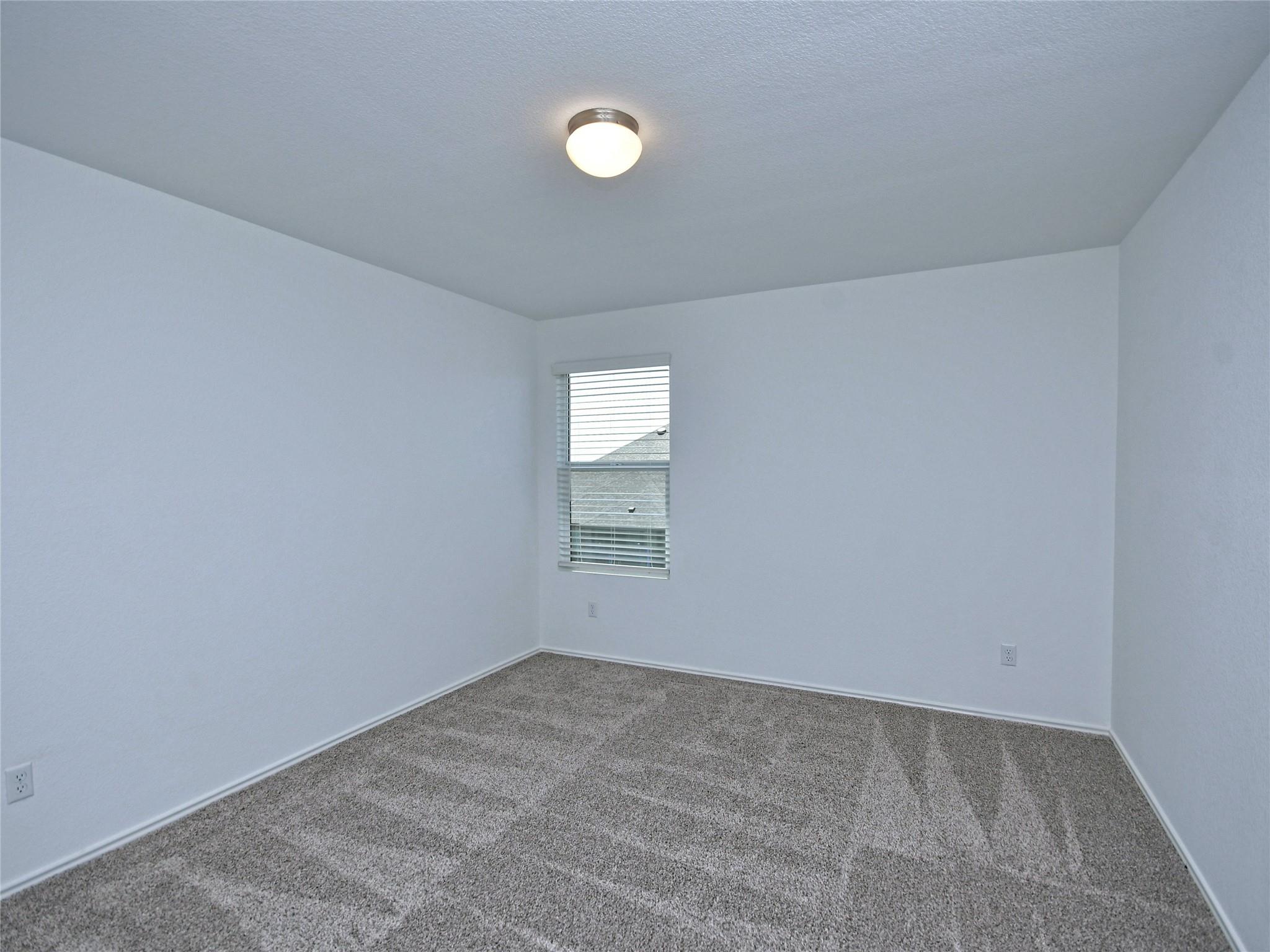 Empty bedroom with gray carpet, white walls, and a window with blinds.