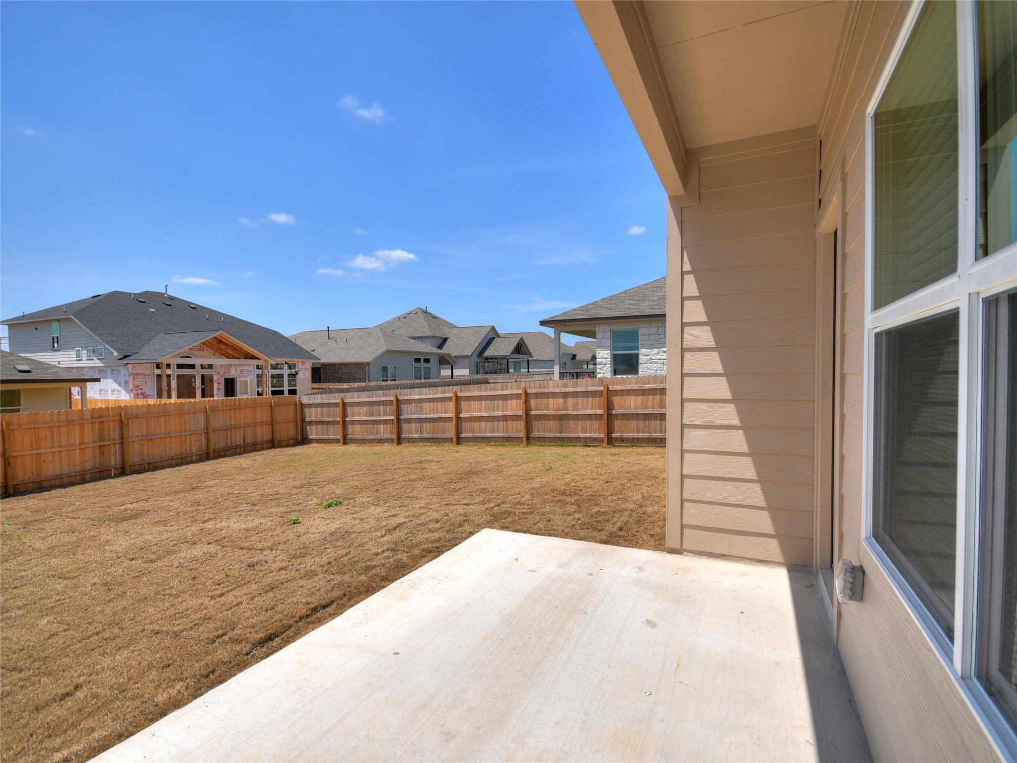 Concrete patio beside a dry, fenced backyard with neighboring homes beyond.