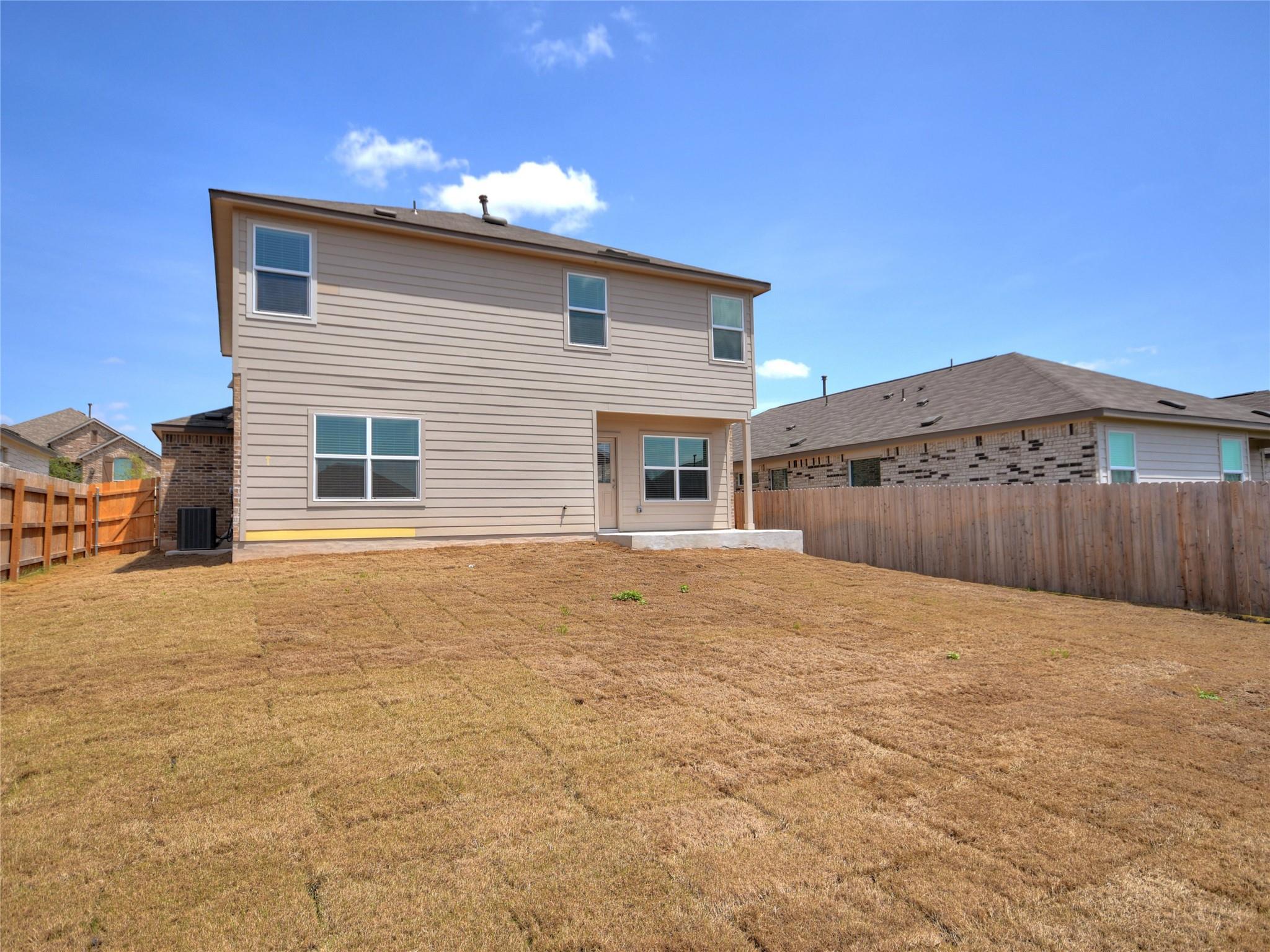 Two-story beige home viewed from its dry, fenced backyard, with a small covered patio.