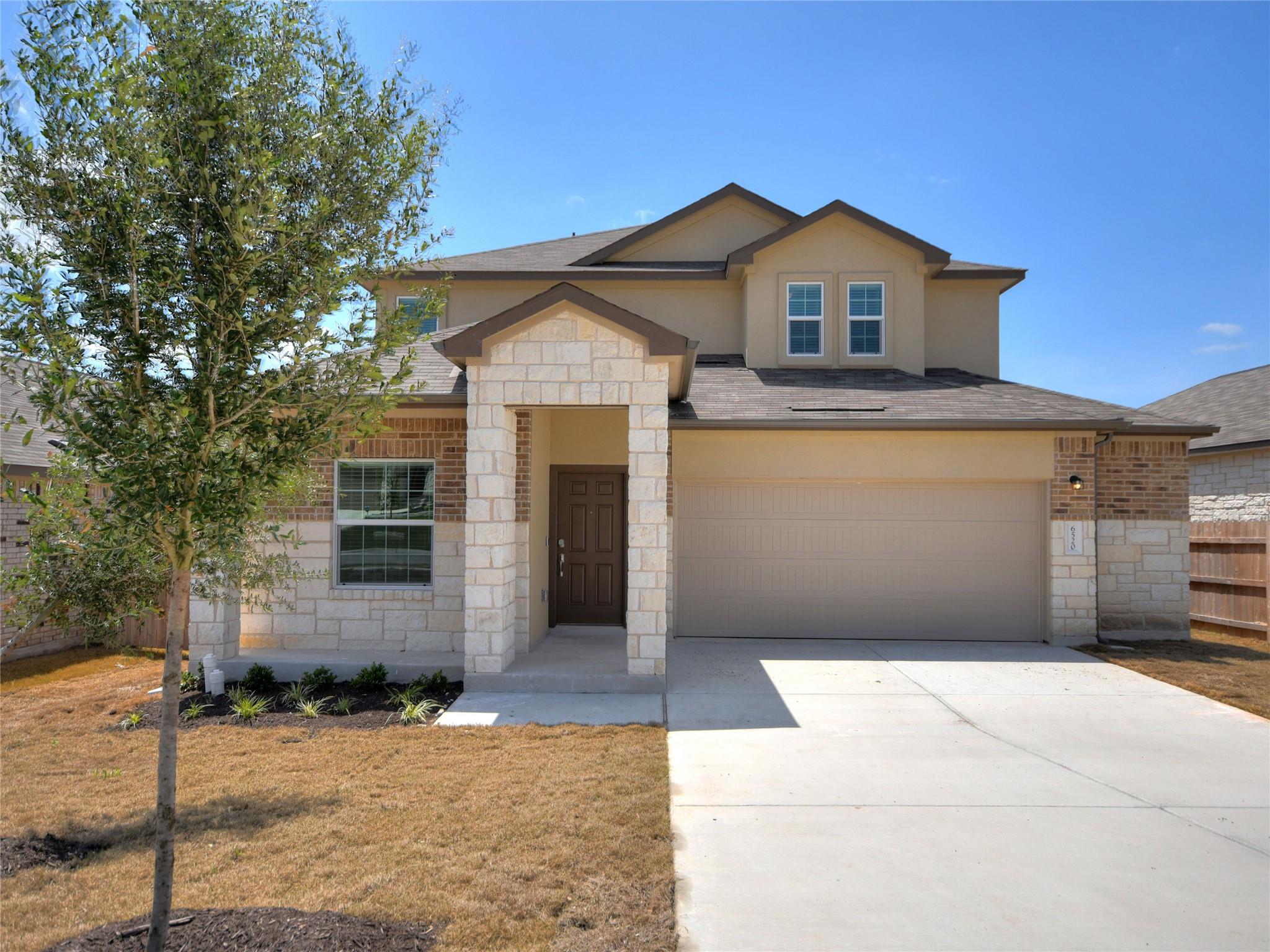 Two-story tan house with a stone entry, brick facade, and attached double garage.