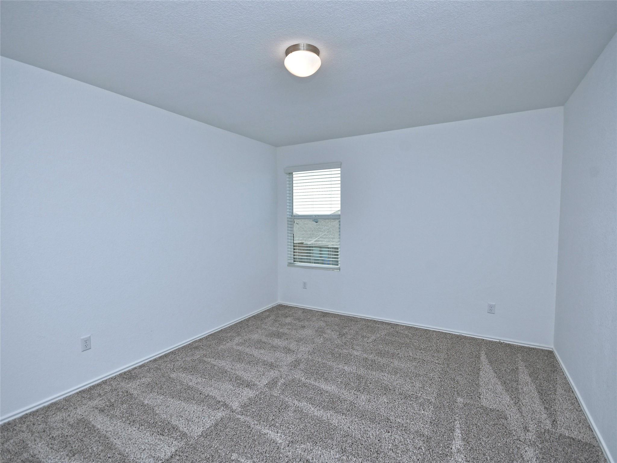 Empty carpeted room with white walls, a window with blinds, and a ceiling light.
