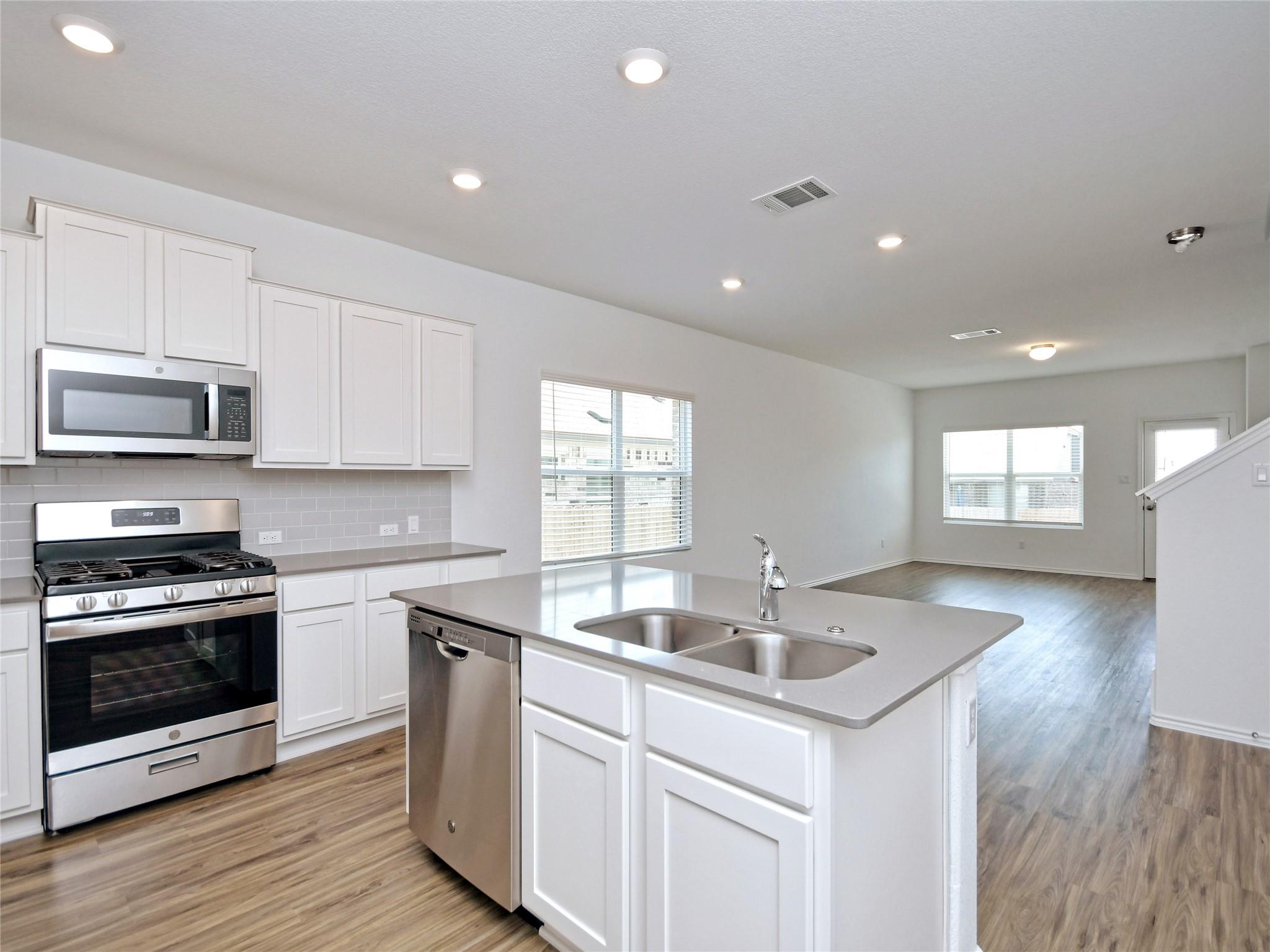 Vacant kitchen with white cabinets, stainless steel appliances, and a large island with a double sink.