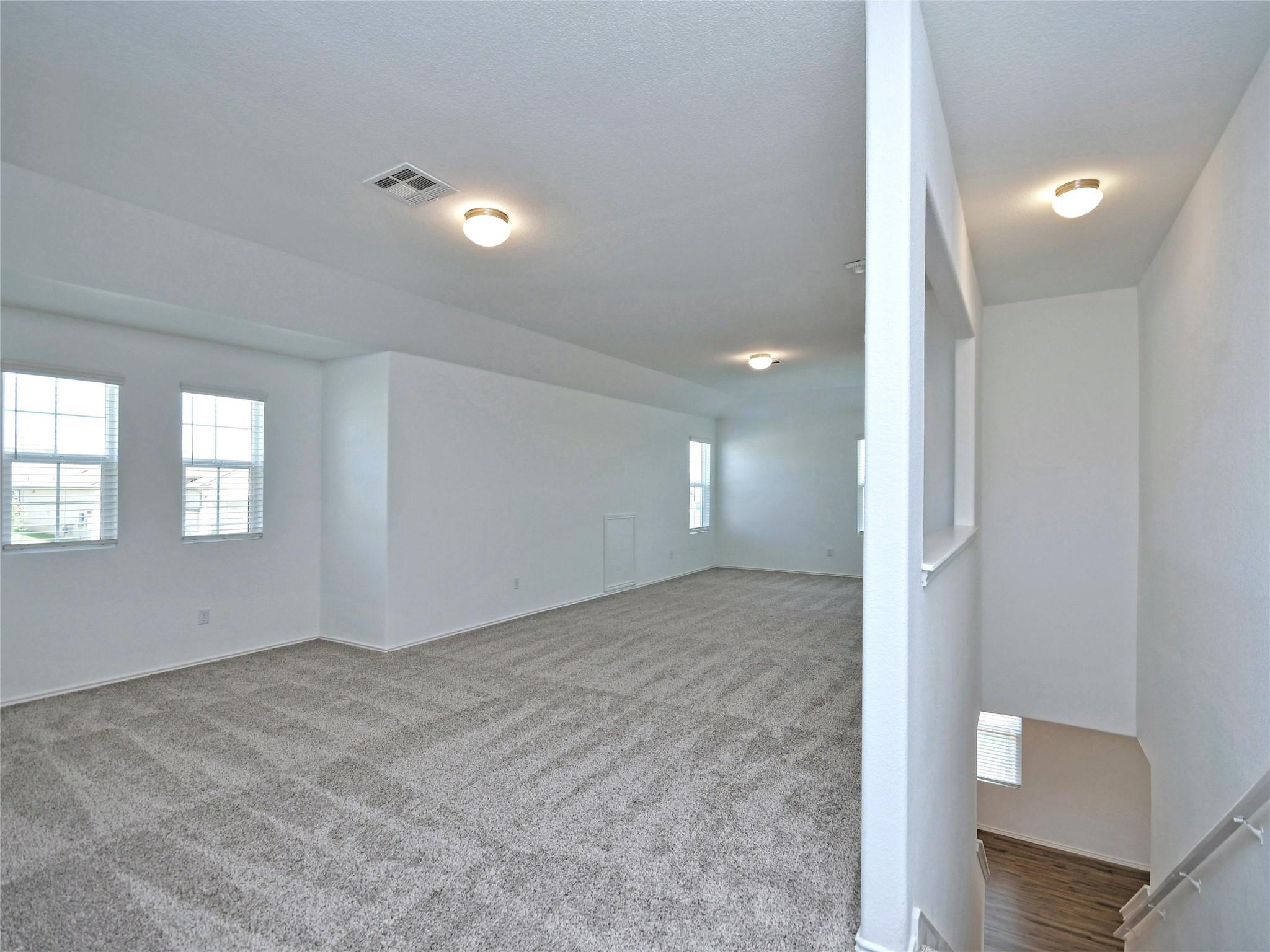 Empty upstairs loft with gray carpet, multiple windows, and a staircase descending to the lower level.