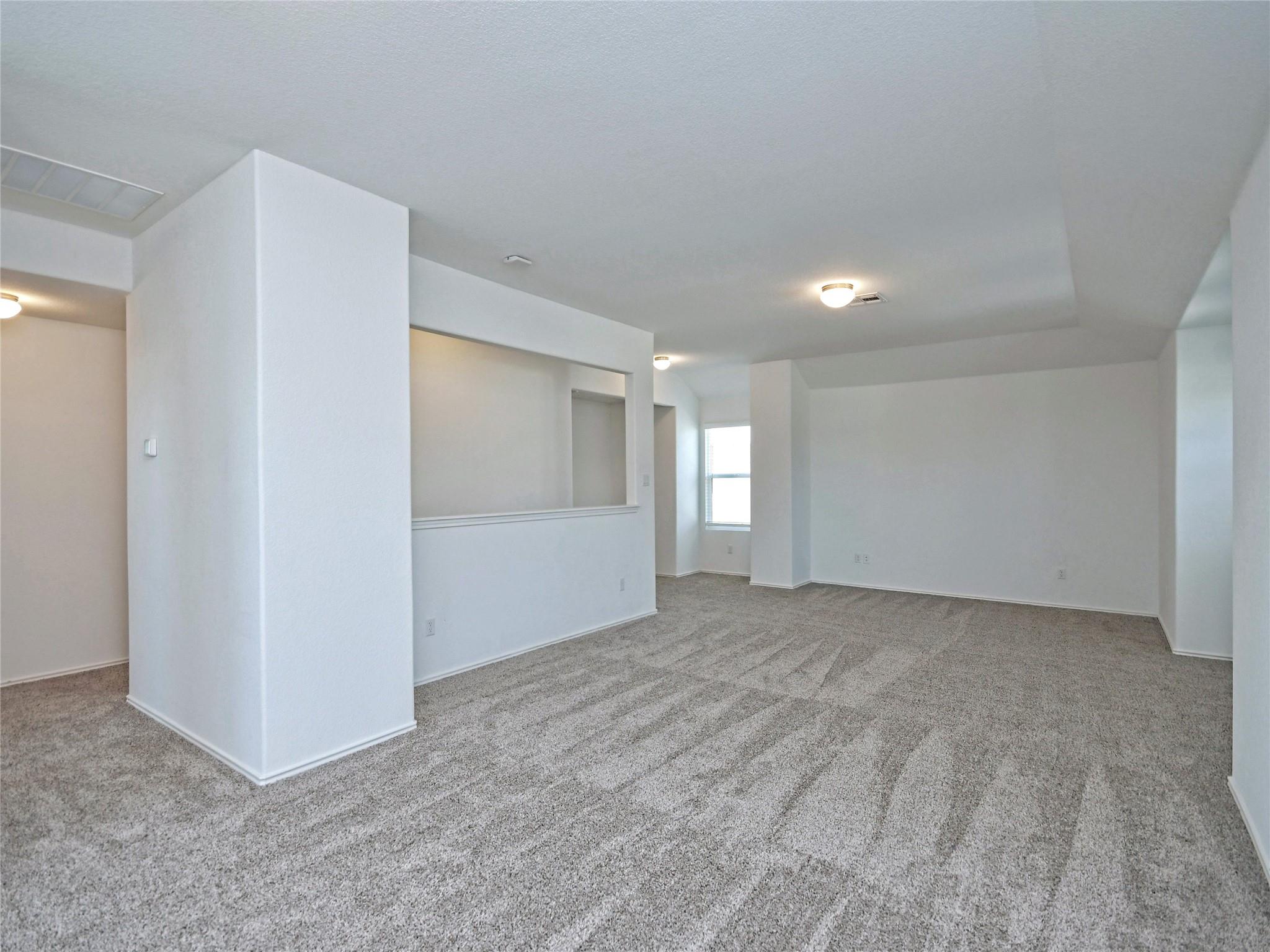 Empty carpeted living area with a pass-through opening and a small rear window.