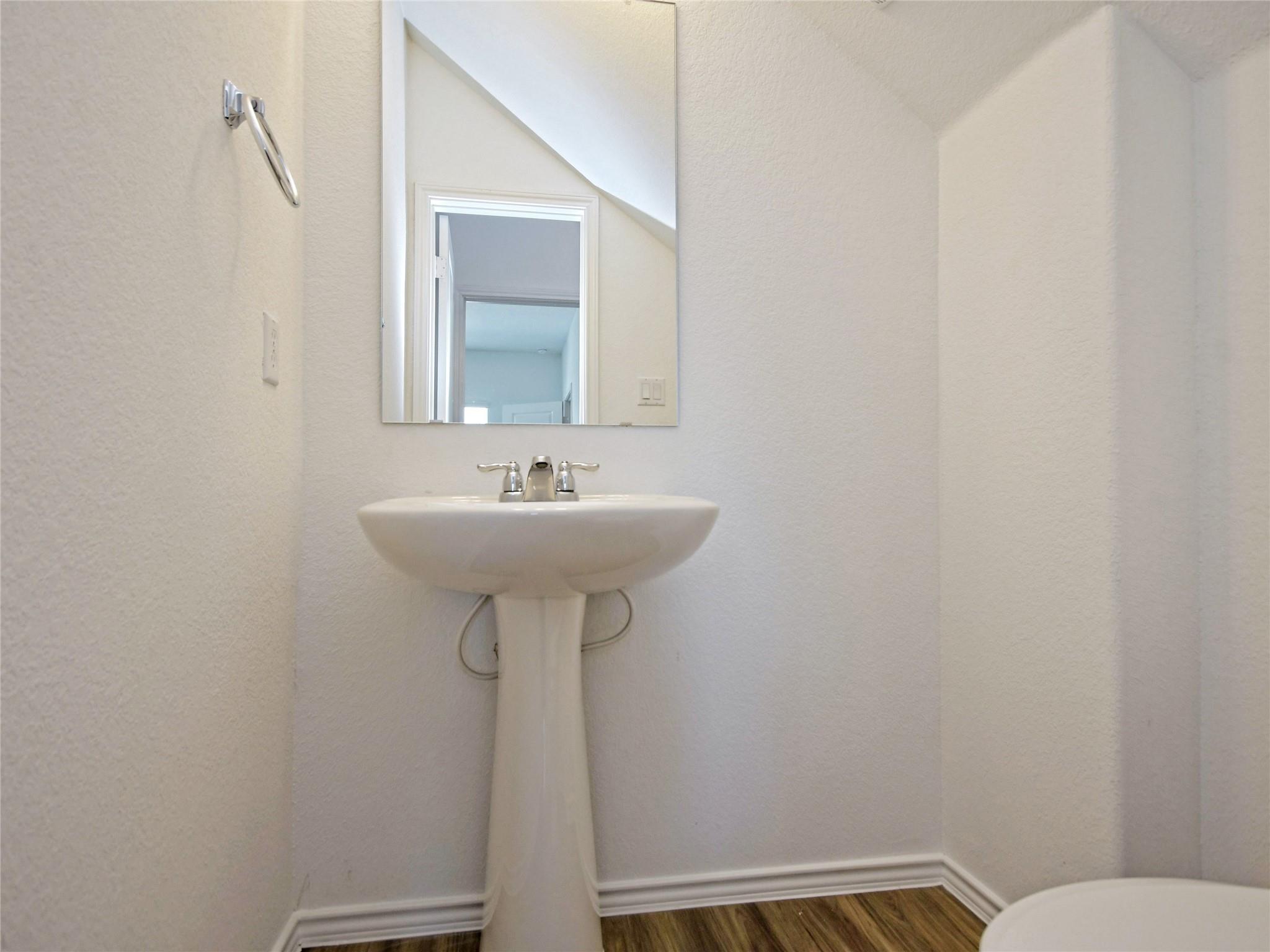 Bathroom with a white pedestal sink, large mirror, wall-mounted towel holder, and wood-look flooring.