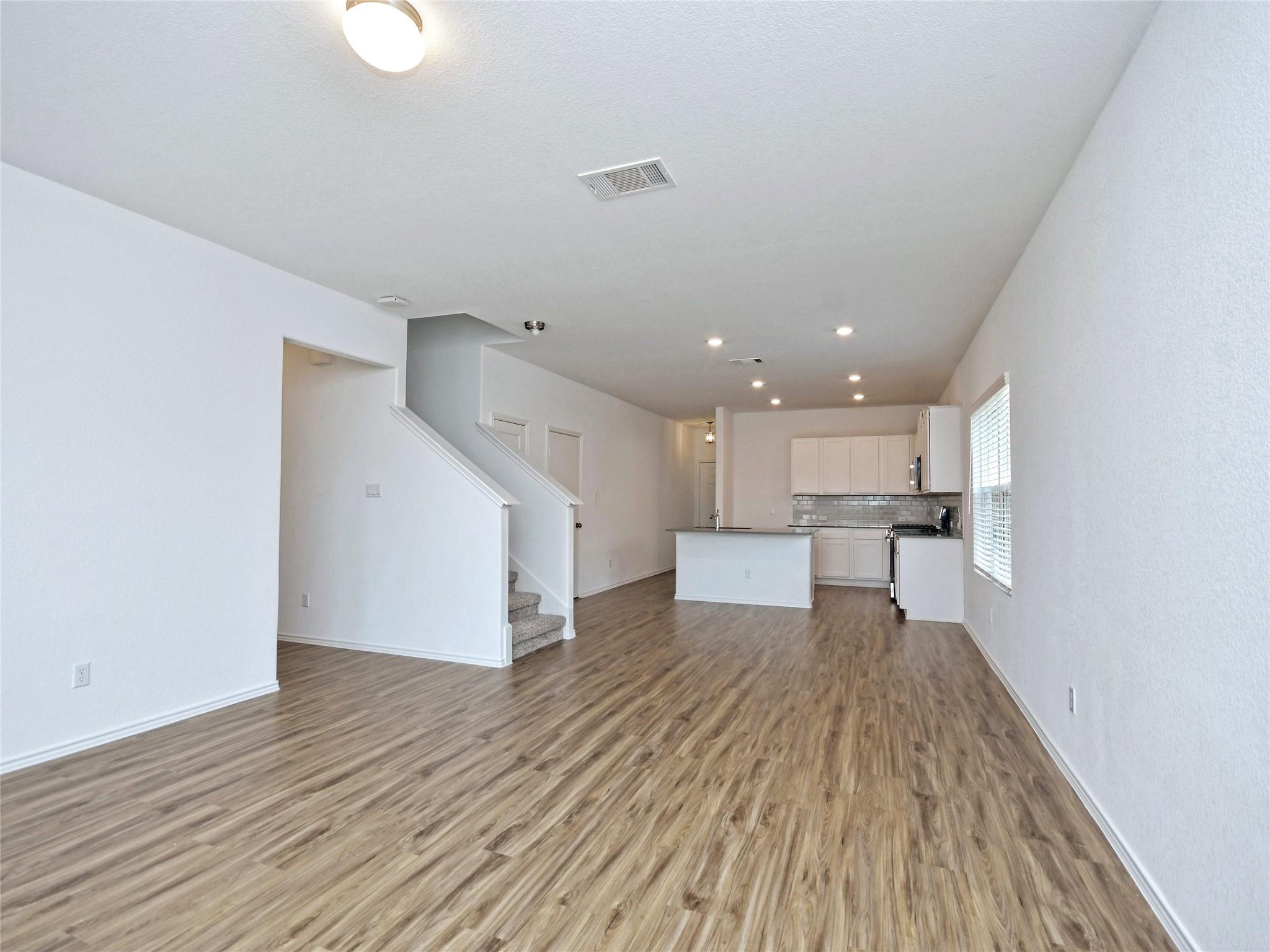 Open-plan living area and kitchen with a central island, wood-look floors, and stairs.