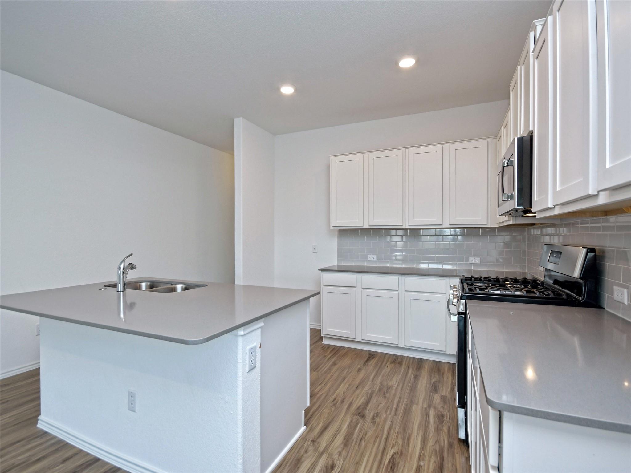 Kitchen with white cabinets, gray tile backsplash, stainless appliances, and a peninsula sink.