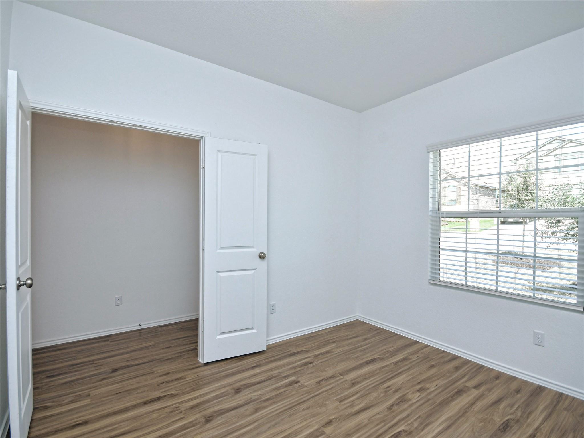 Empty room with wood-look flooring, an open door, and a window with blinds.